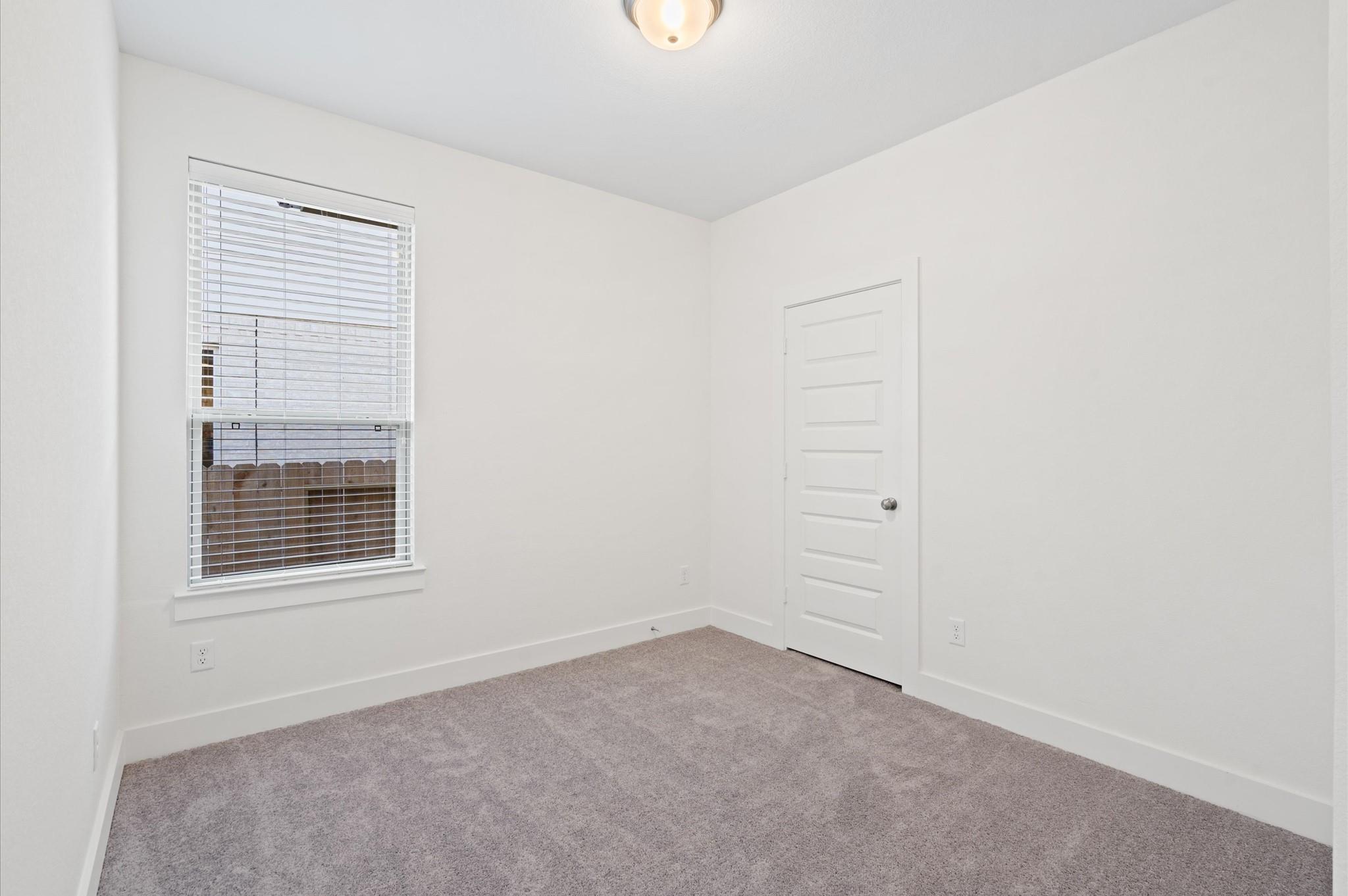 Empty bedroom with gray carpet, a window with blinds, and a white paneled door.