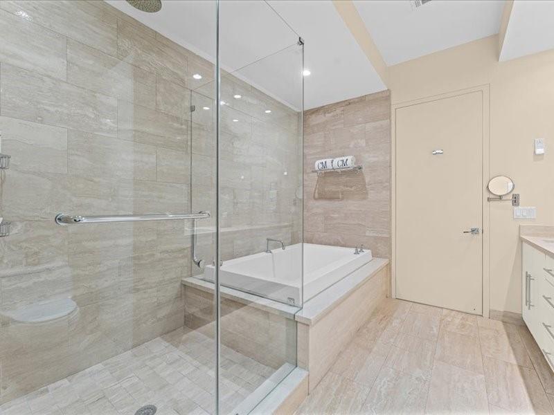 Bathroom with a glass-enclosed shower, rectangular soaking tub, and pale stone tile.