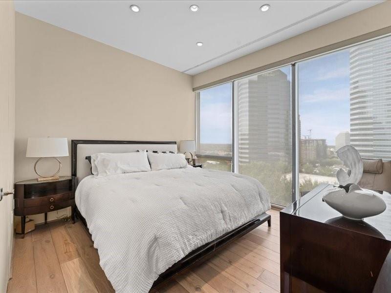Bedroom with a large bed beside floor-to-ceiling windows overlooking high-rise buildings.
