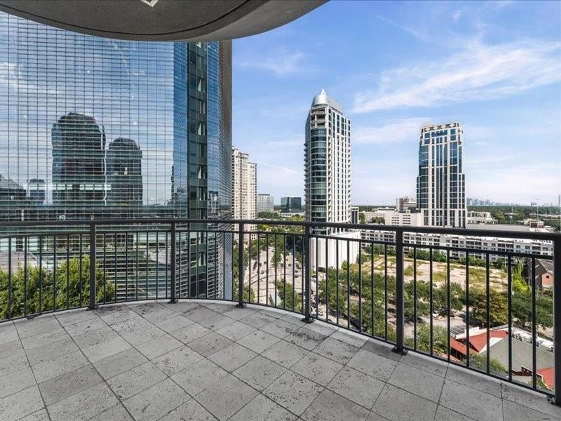 High-rise balcony with tiled flooring and black railings overlooking Houston’s downtown towers.