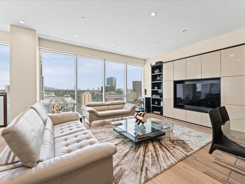 High-rise living room with white leather sofas and floor-to-ceiling windows overlooking the city skyline.