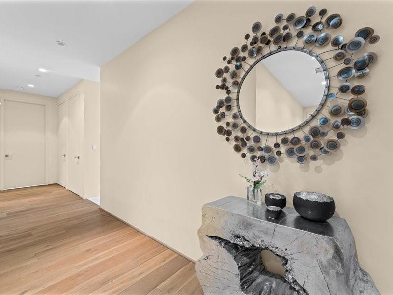 Condominium entry hall with light wood floors, a sculptural stone console, and an ornate round mirror.