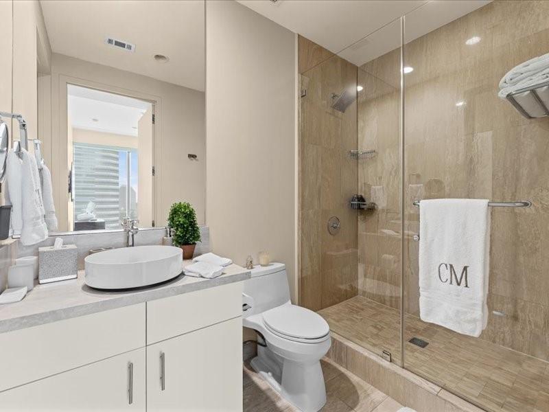 Condo bathroom with a round vessel sink, white vanity, and beige-tiled glass shower.
