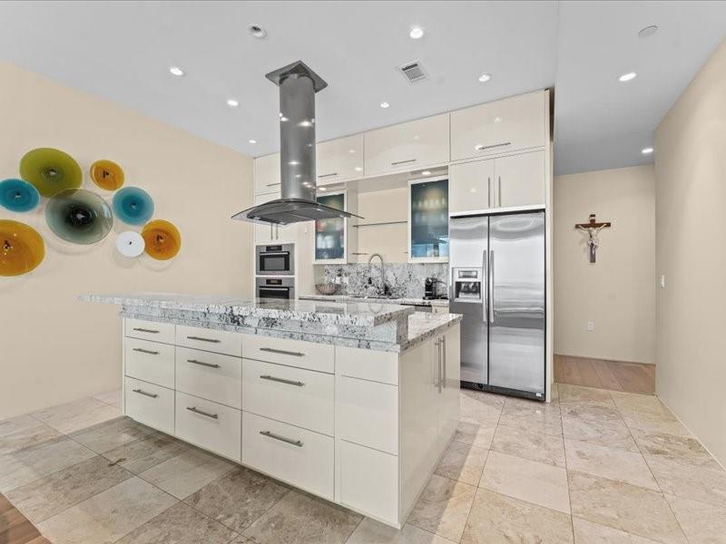 Modern kitchen with a large stone island, white cabinets, and stainless steel appliances.