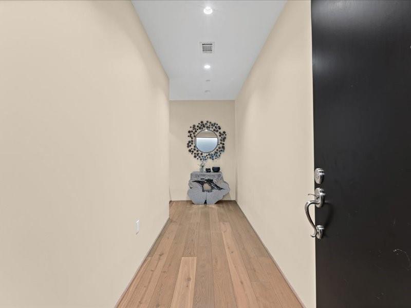 Apartment entry hallway with hardwood floors and a console table beneath a round mirror.