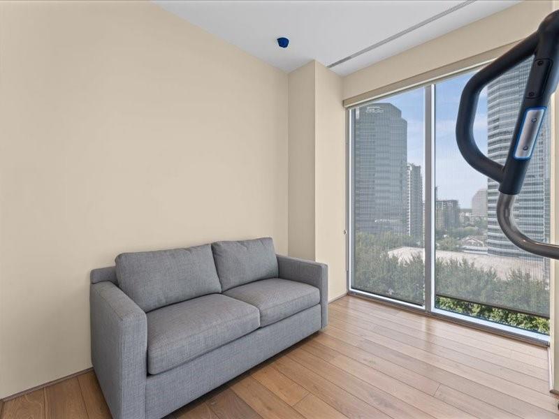 Furnished room with a gray sofa, wood flooring, and floor-to-ceiling windows overlooking the city skyline.