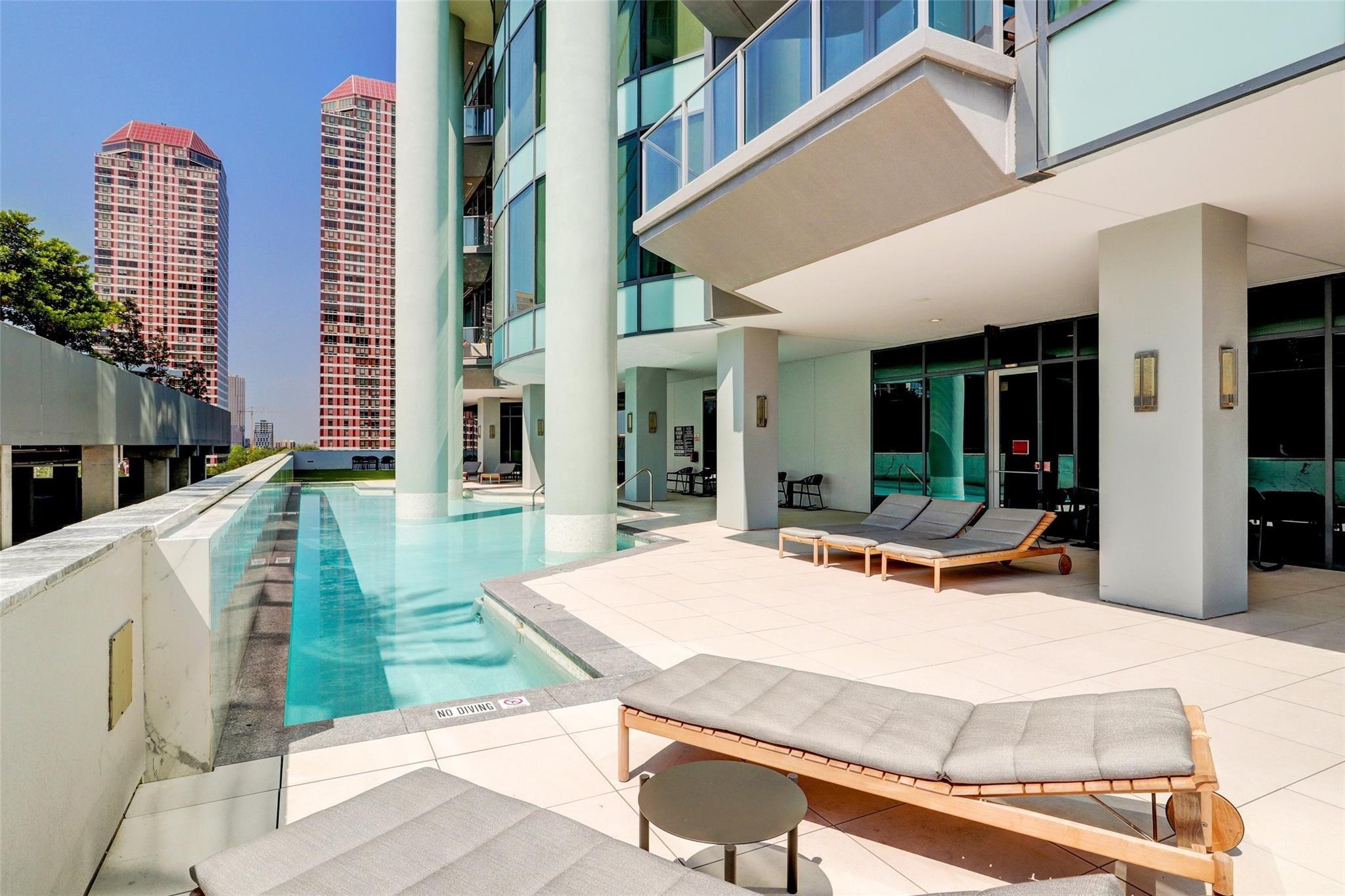 High-rise pool deck with turquoise water, cushioned loungers, and city towers beyond.