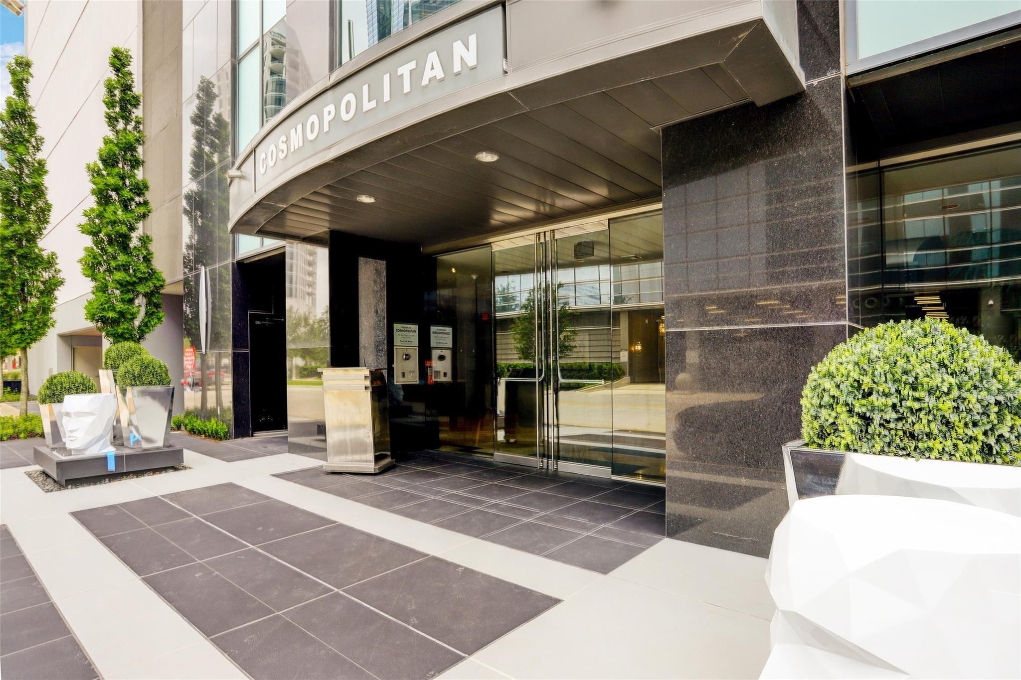 Cosmopolitan condominium entrance with a curved sign canopy, glass doors, and landscaped planters.