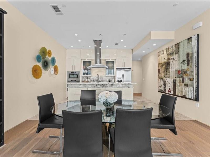 Dining area with a round glass table and dark chairs opening into a white modern kitchen.