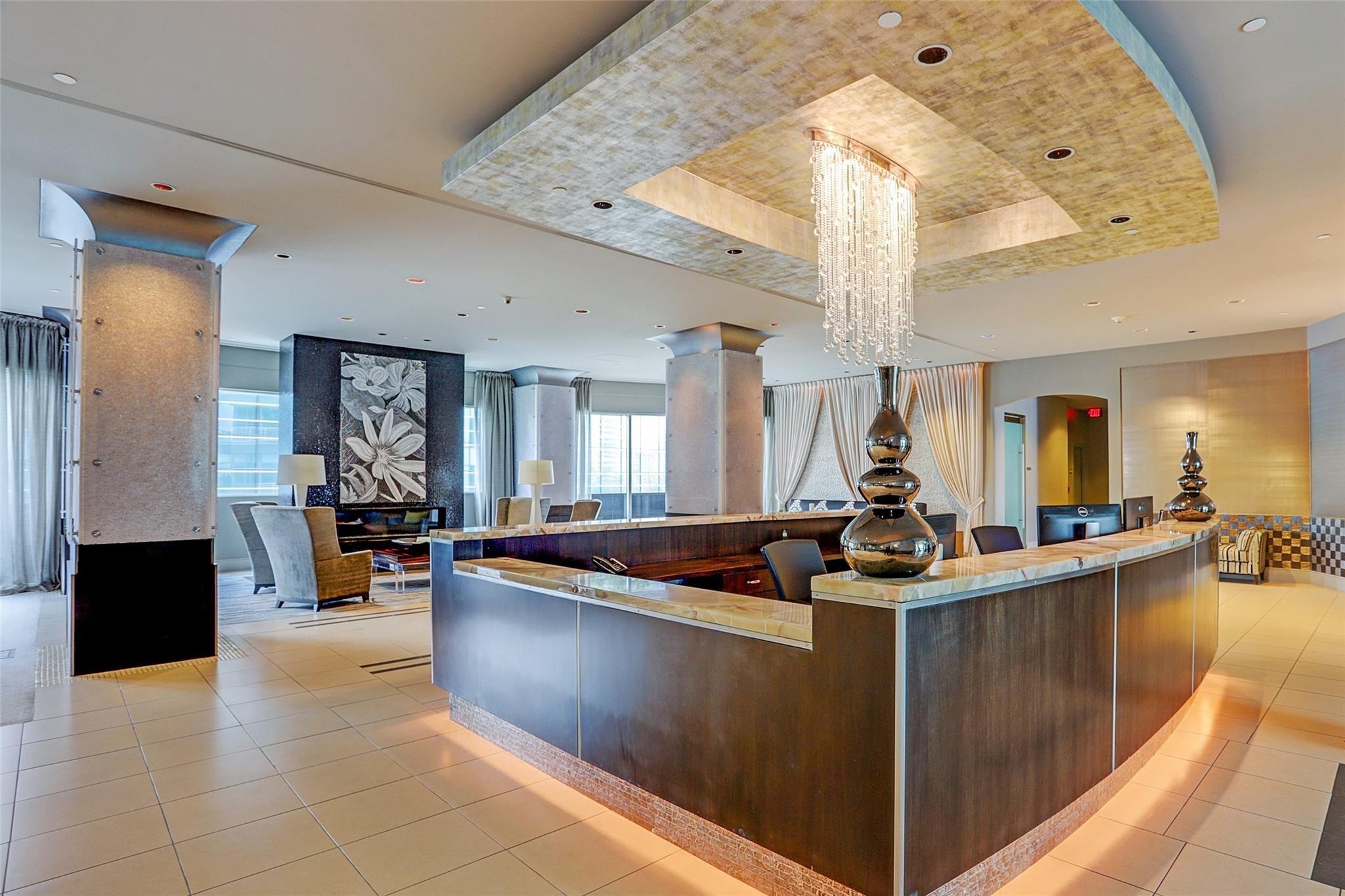 Residential lobby with a curved reception desk, crystal chandelier, and lounge seating.