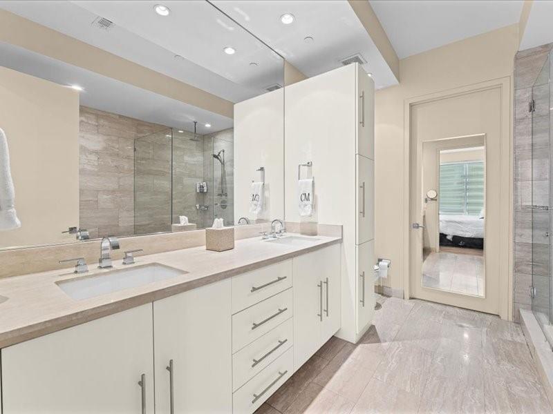 Bright bathroom with a long white vanity, wide mirror, and glass-enclosed tiled shower.