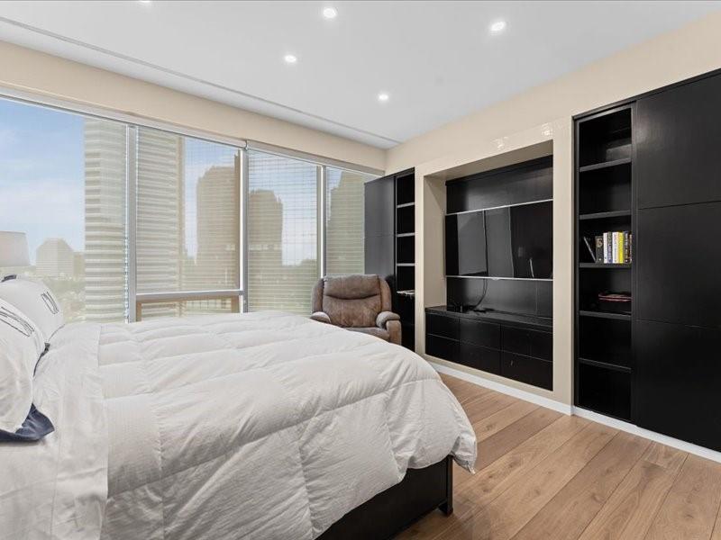 Bedroom with floor-to-ceiling windows overlooking the city and built-in shelving around a television.