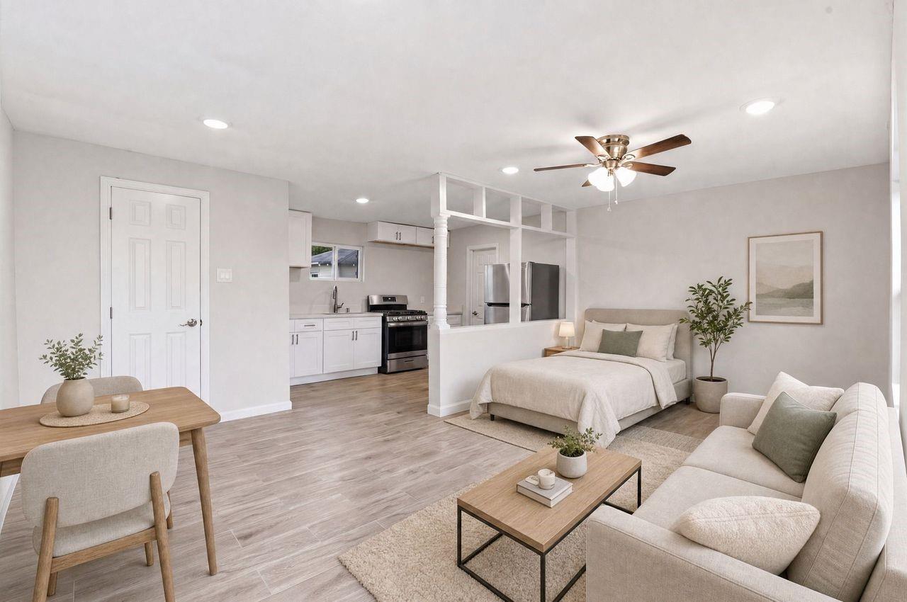 Staged open-plan studio with a bedroom behind a low divider and a bright white kitchen.