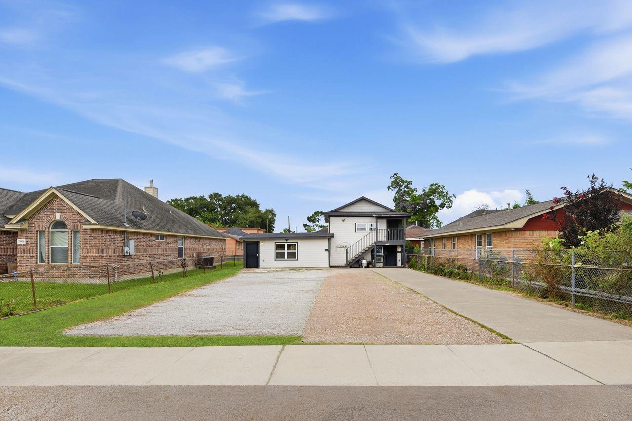 White two-story home at the end of a gravel driveway, with exterior stairs and brick neighbors.