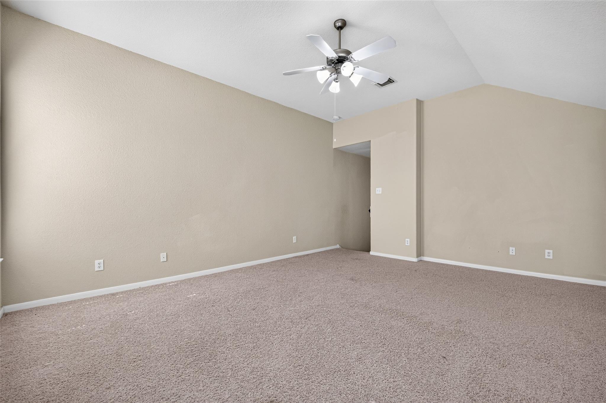 Empty beige room with carpet, high ceiling, and a ceiling fan with lights.