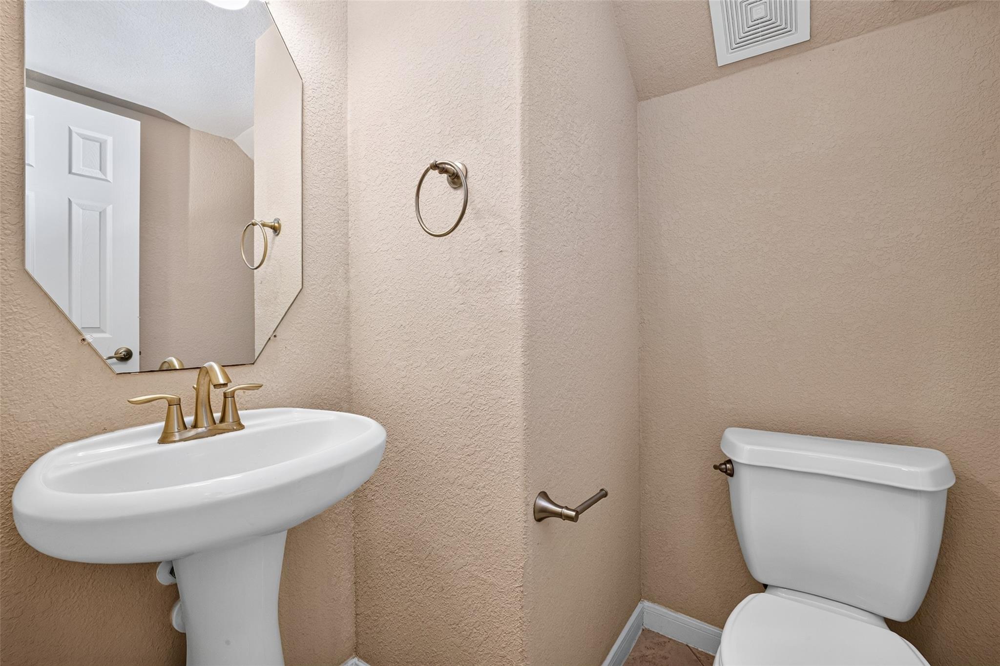 Powder room with a white pedestal sink, toilet, large mirror, and brass-toned fixtures.