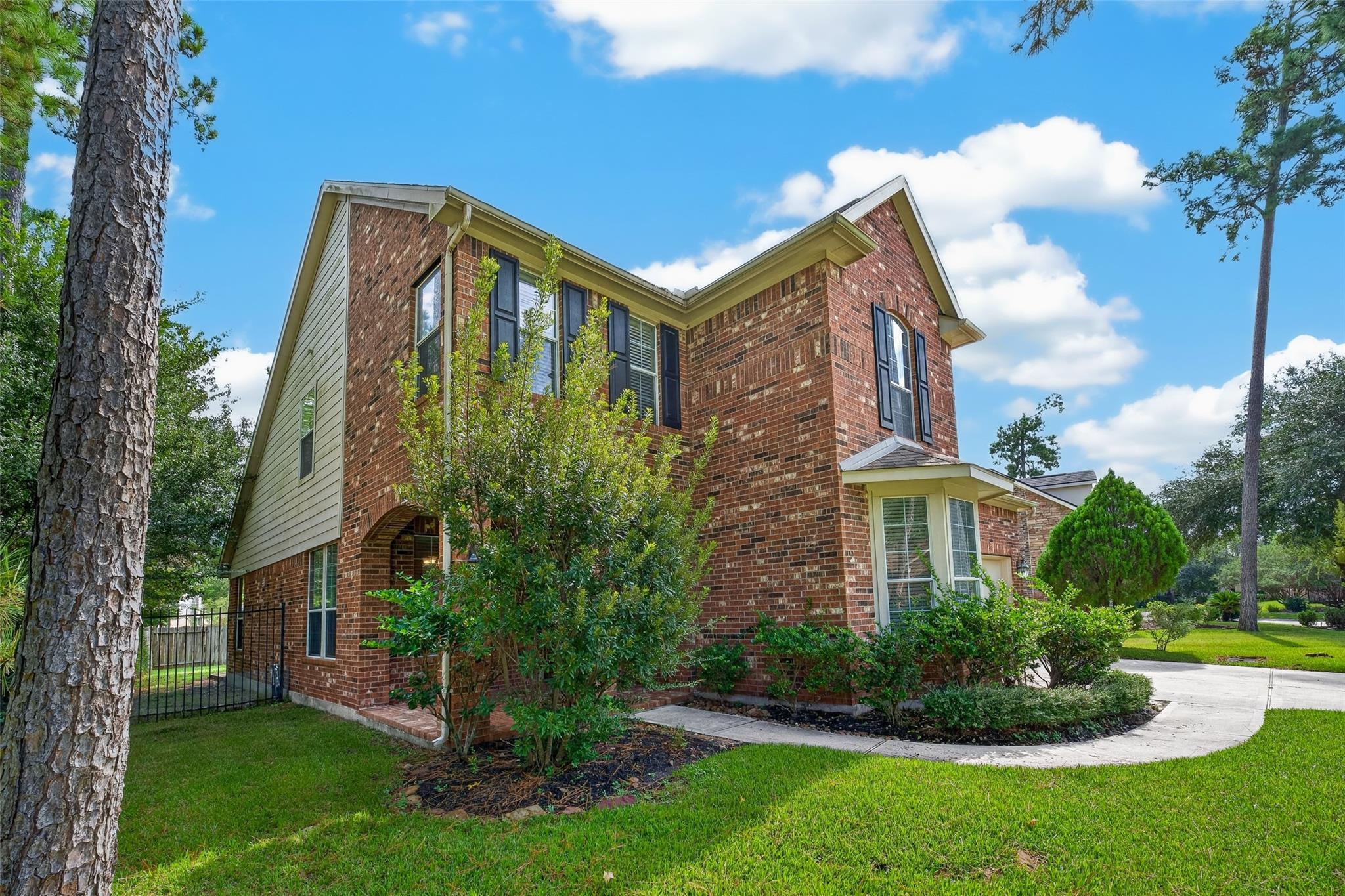 Two-story brick house framed by mature trees, with landscaped shrubs and a curved walkway.