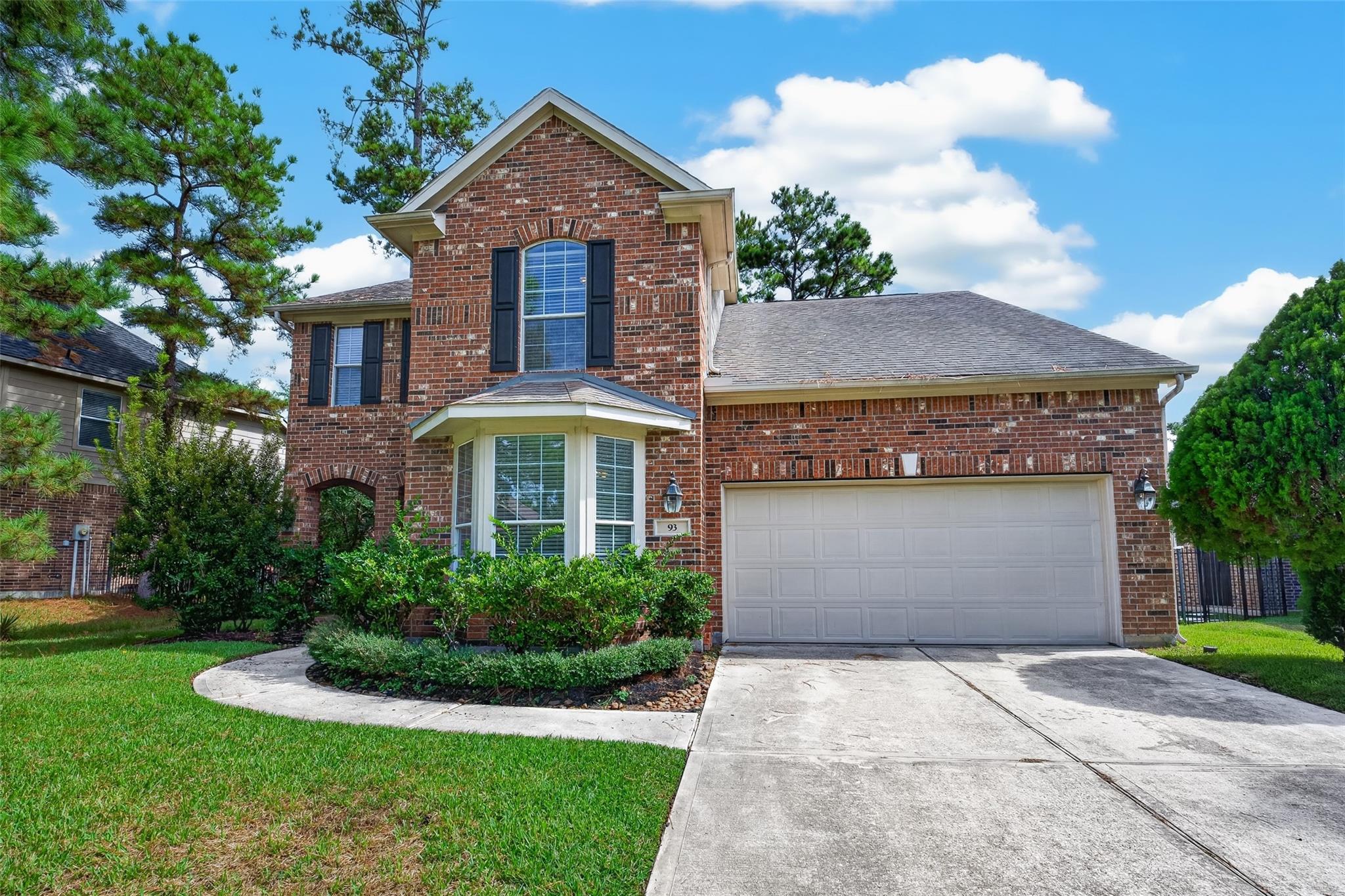 Two-story red brick house with a bay window, double garage, and landscaped front yard.