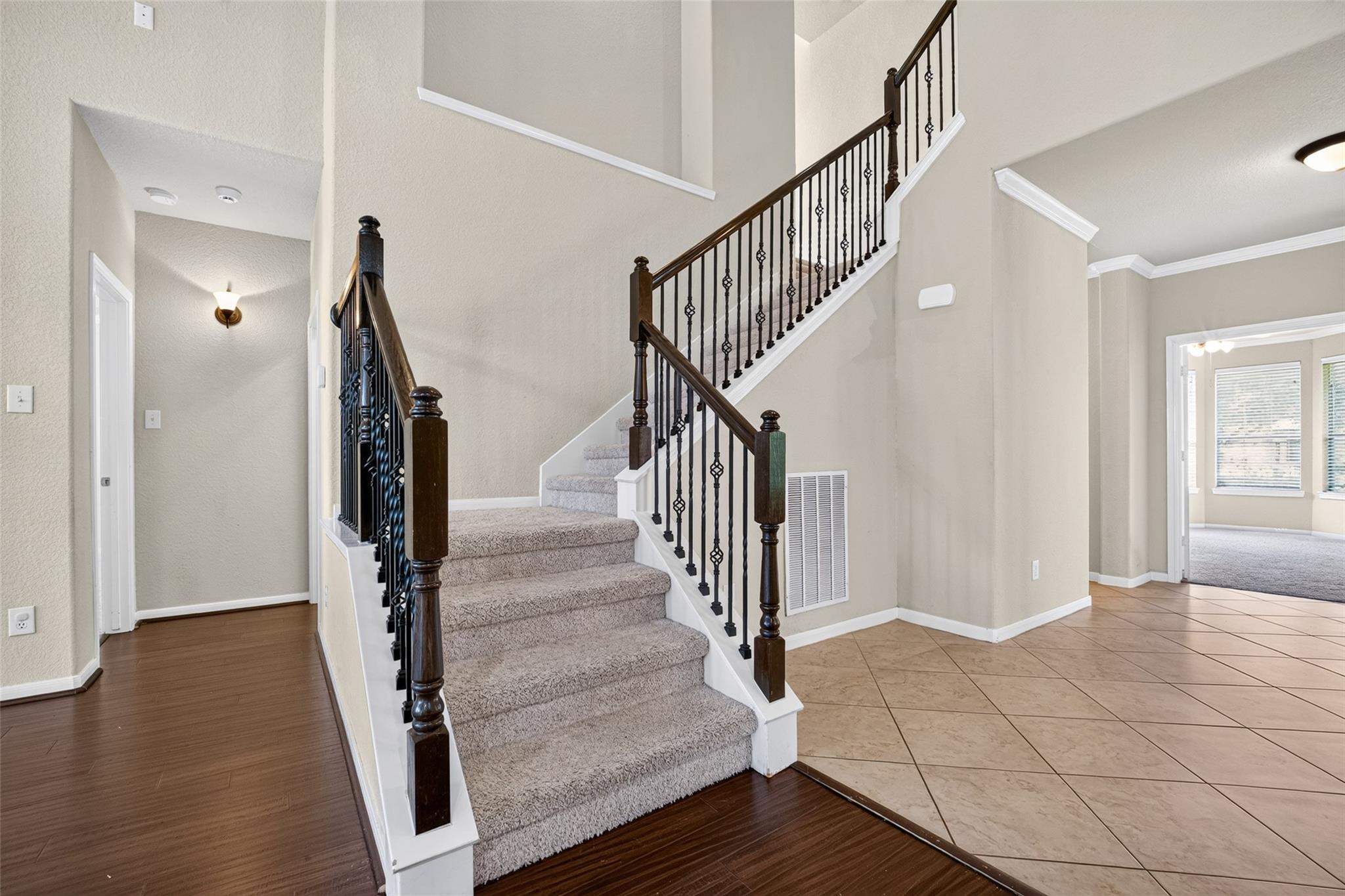 Foyer with a carpeted staircase, dark wood handrails, and ornate black metal balusters.