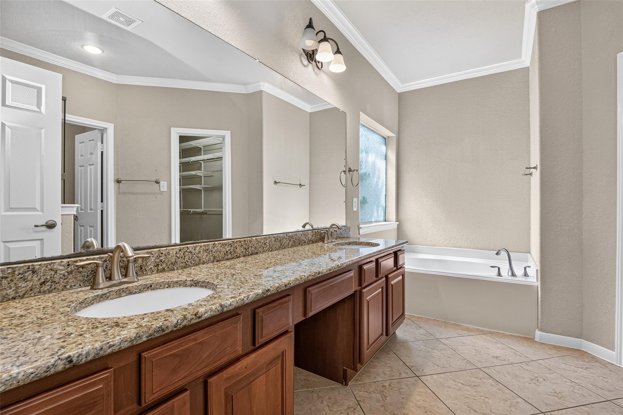 Bathroom with a granite double vanity, dark wood cabinets, and a bathtub beside a window.