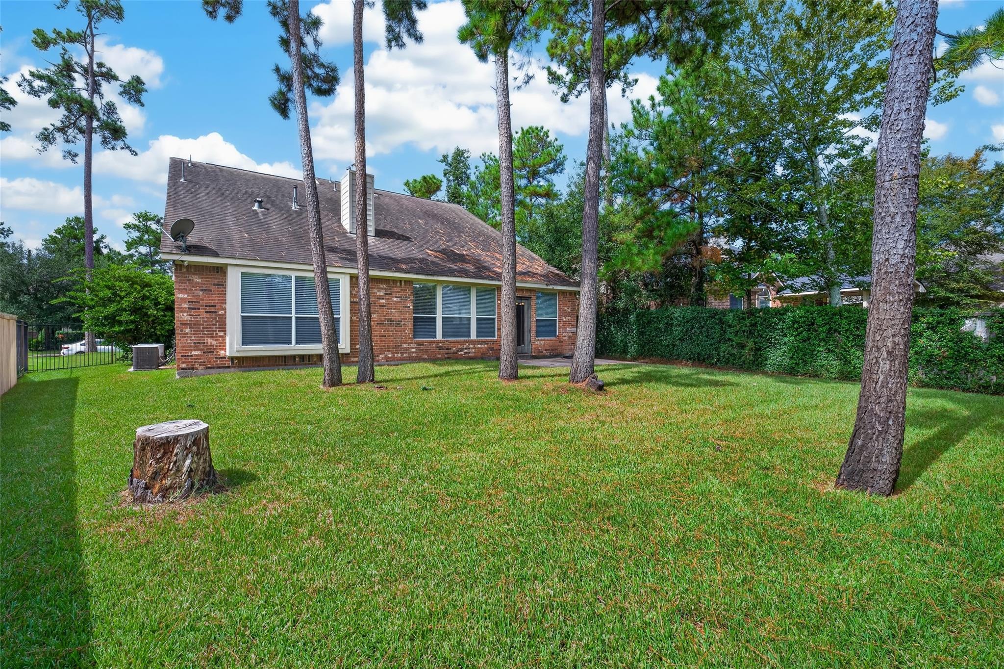 Brick house behind a broad lawn, framed by tall pine trees.