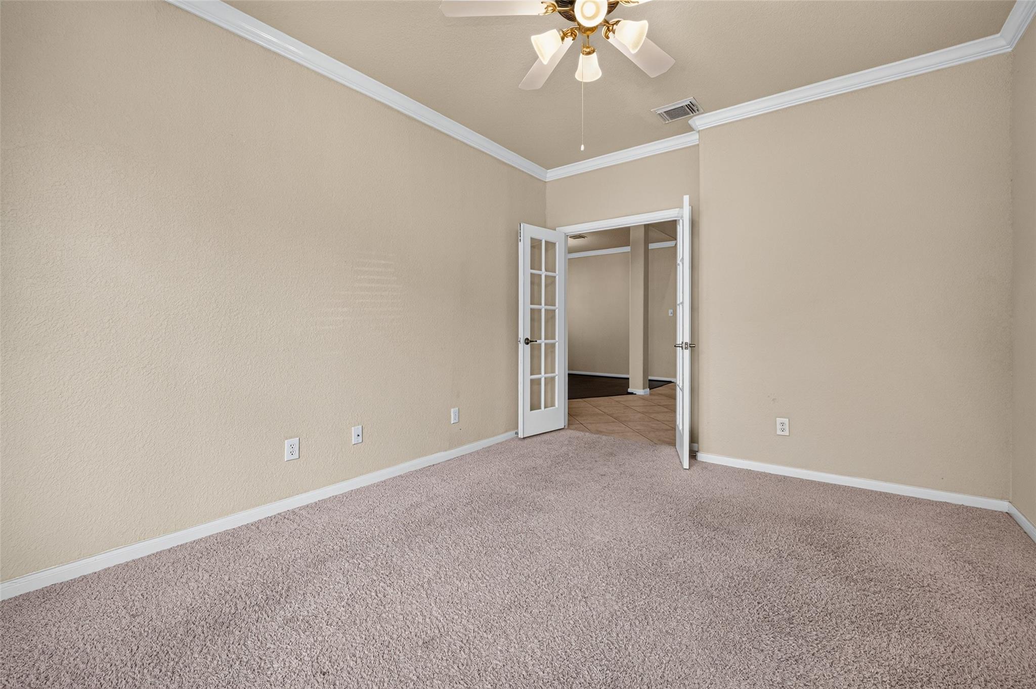 Empty beige bedroom with plush carpet and open French doors to a tiled adjoining area.