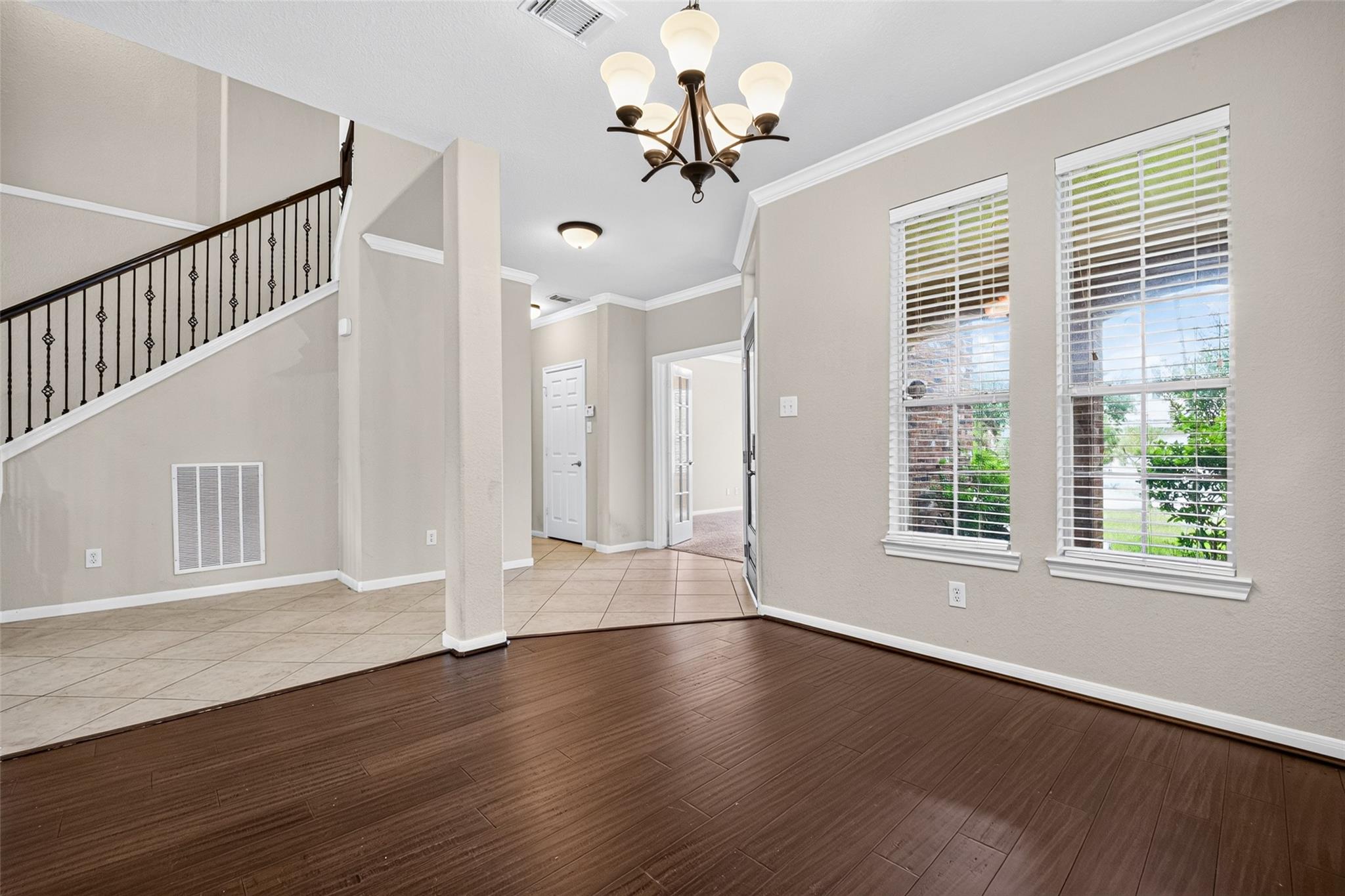 Vacant entry area with tiled flooring, an iron-railed staircase, tall windows, and a chandelier.
