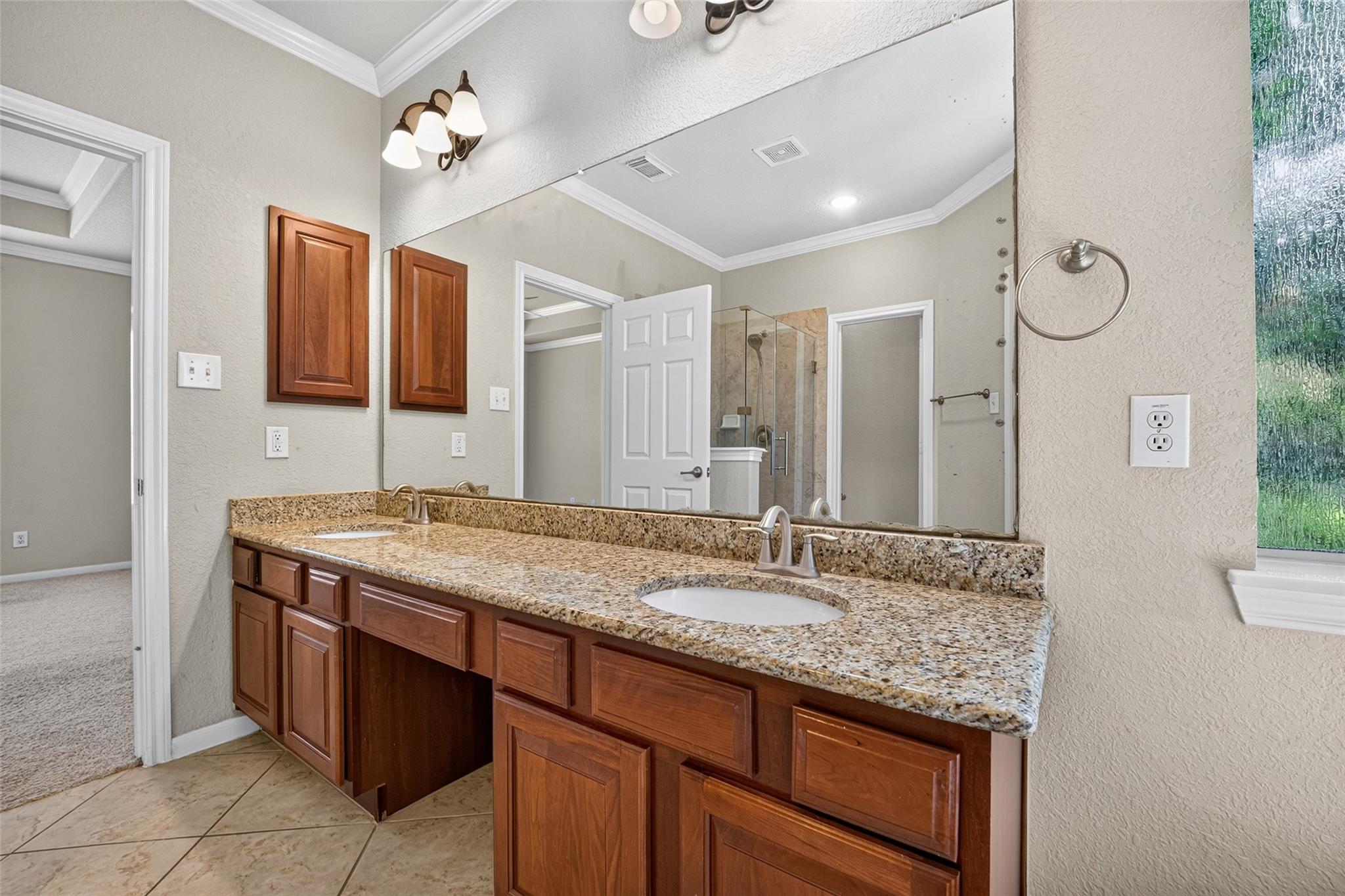 Bathroom vanity with granite countertop, wood cabinets, large mirror, and glass shower.