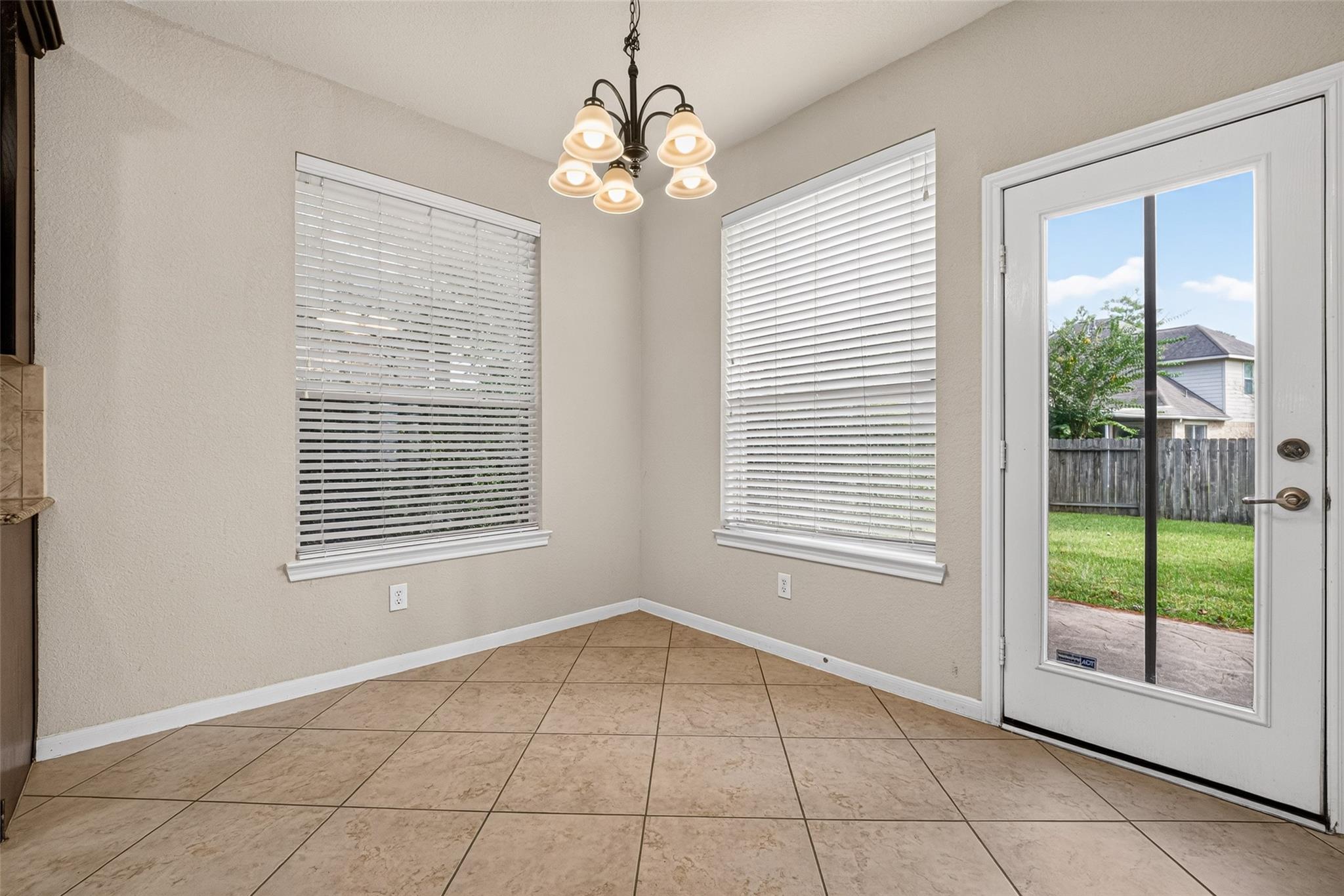 Empty dining nook with tile flooring, two blinded windows, and a glass patio door to the backyard.