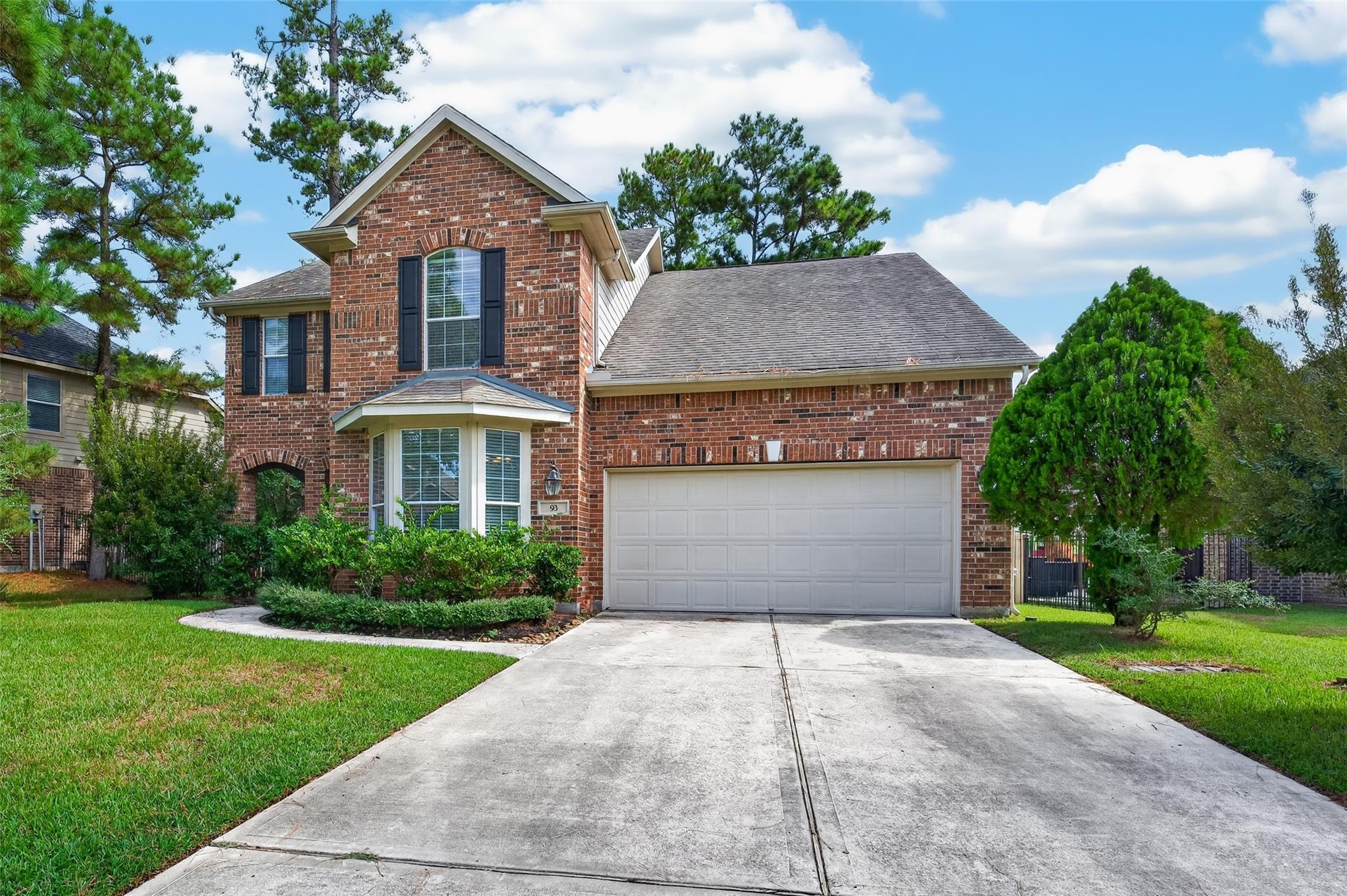 Two-story brick house with a white double garage, bay window, and broad concrete driveway.