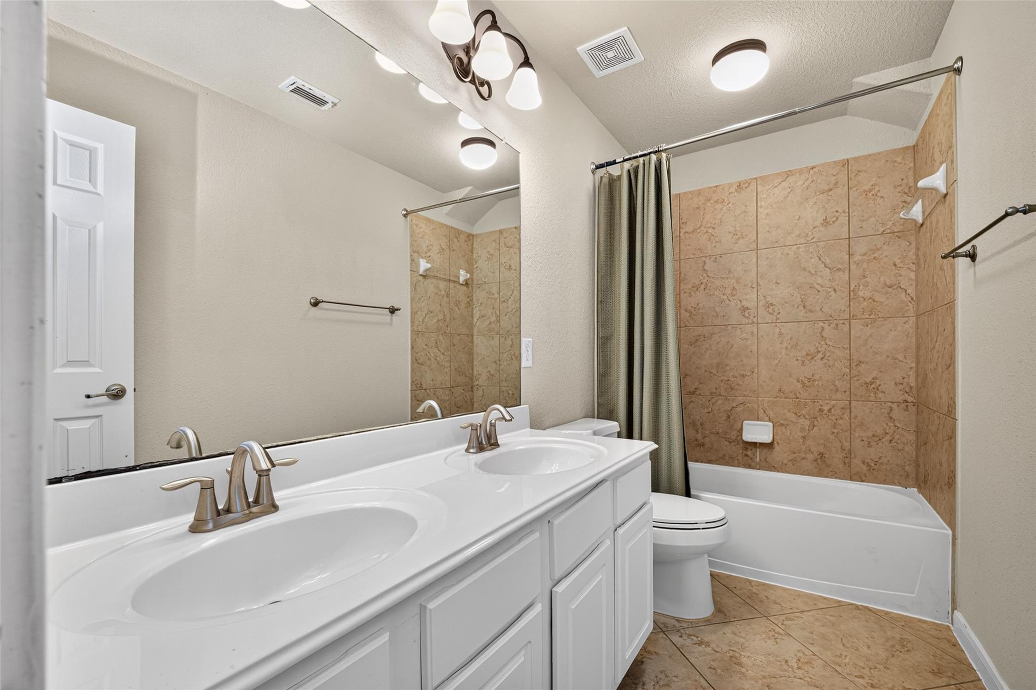 Bathroom with a double-sink vanity and tan tile surrounding the bathtub and shower.