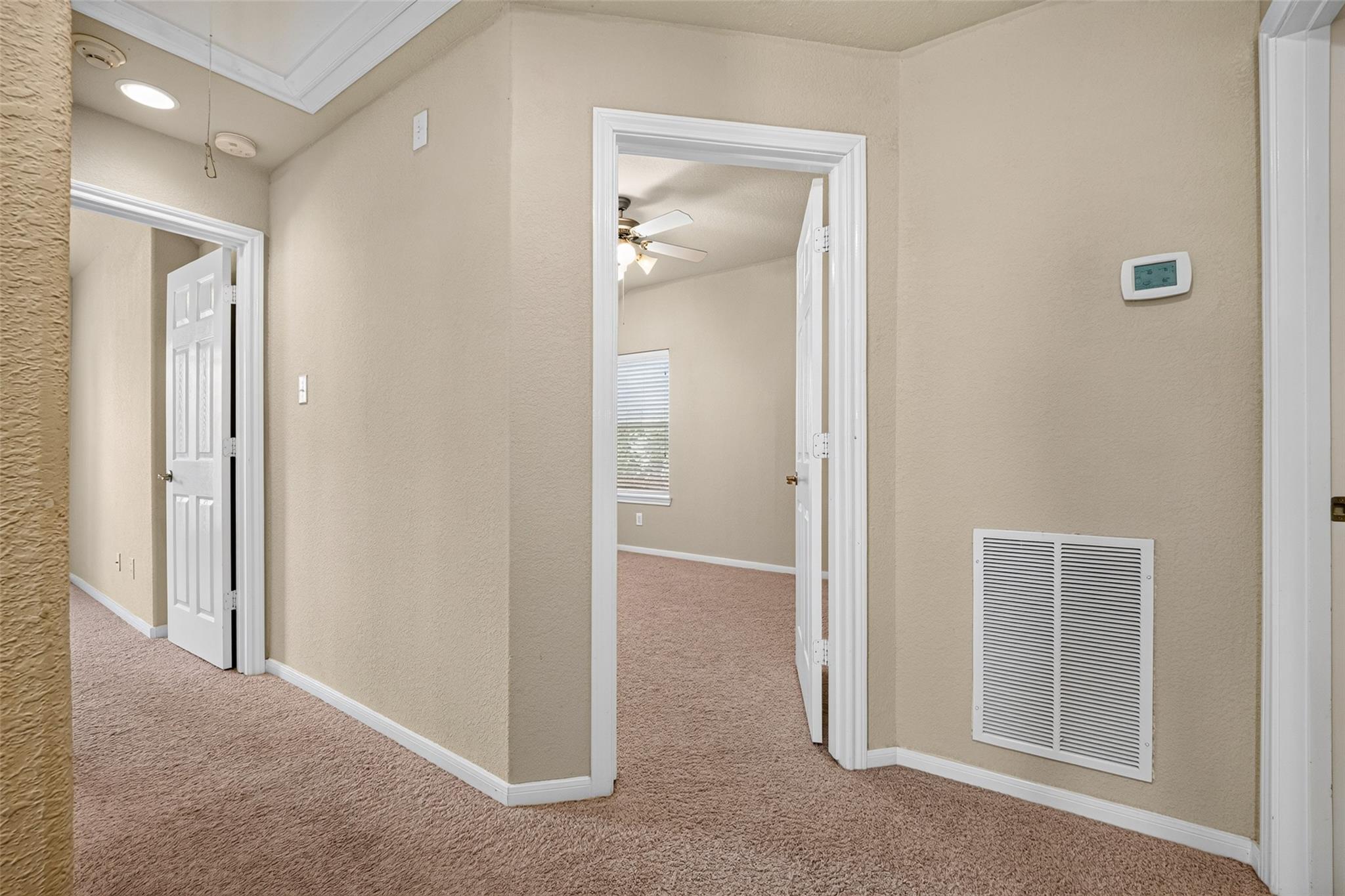 Carpeted hallway with open doorways, white trim, and a large wall air return vent.