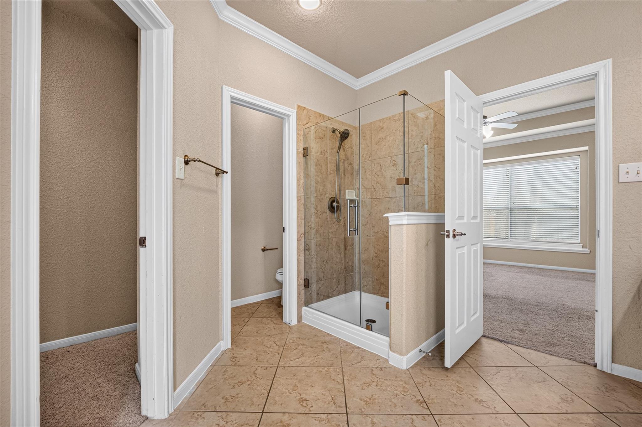 Bathroom with a glass-enclosed tan tile shower and an open doorway to a carpeted room.