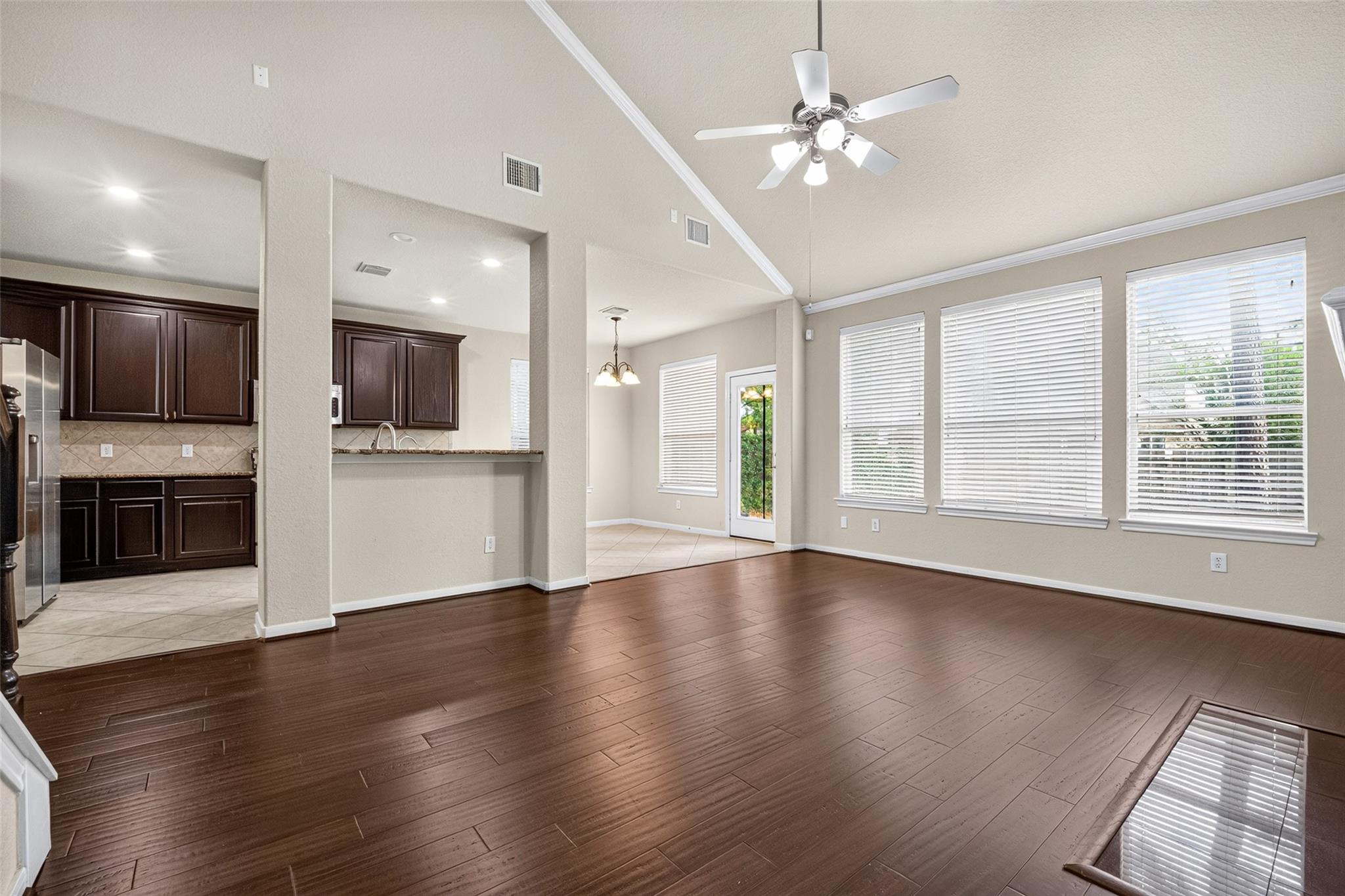 Open living and dining area with dark wood floors, large windows, and an adjoining kitchen.