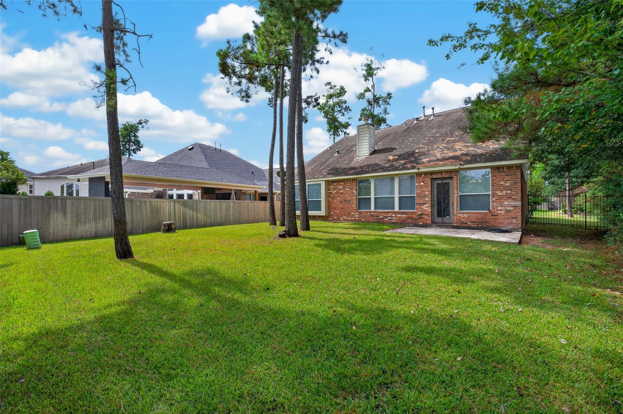 Brick home’s rear exterior with a fenced grassy yard and tall pine trees.
