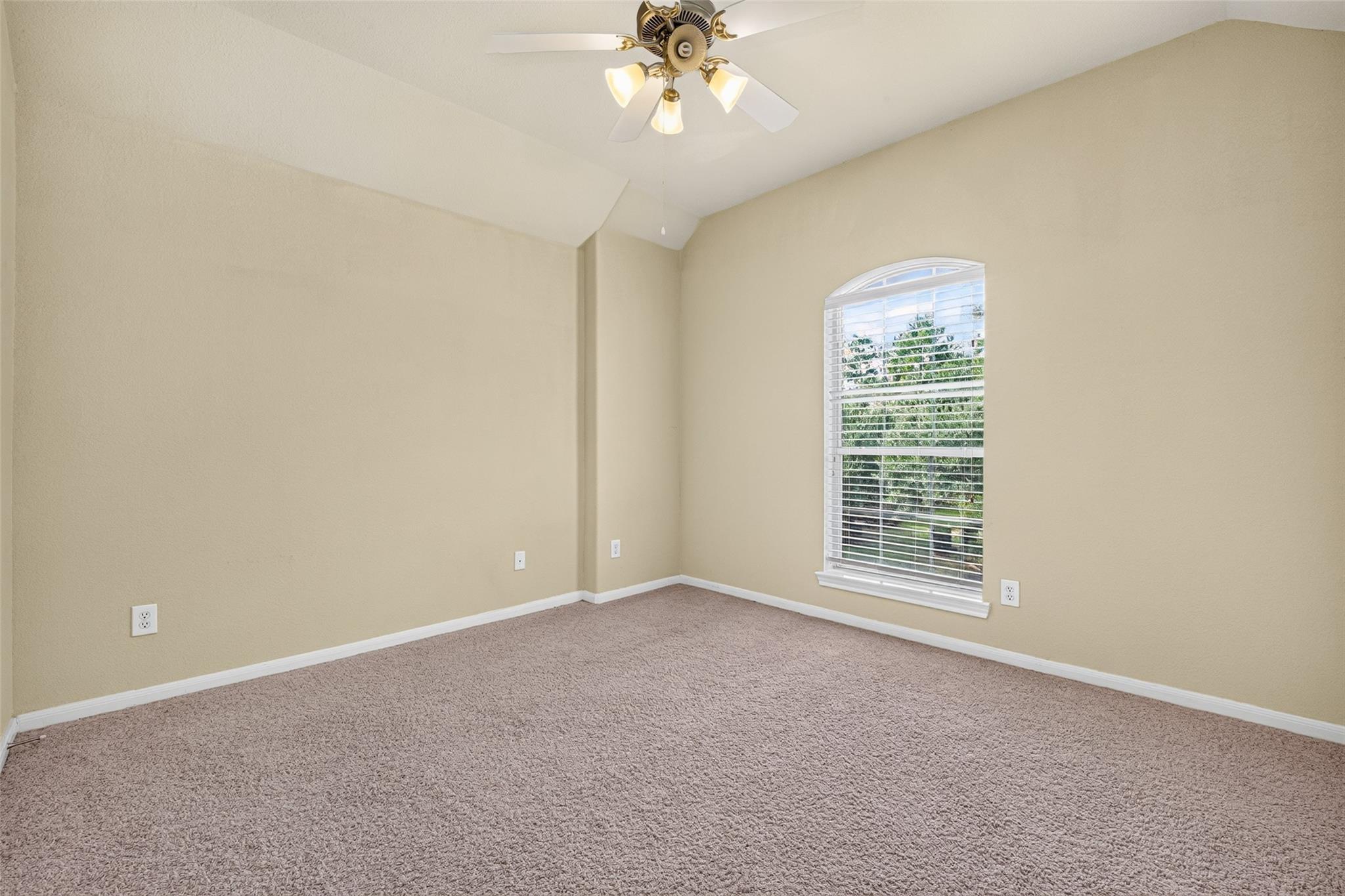 Empty bedroom with vaulted ceiling, carpet, ceiling fan, and arched window with blinds.