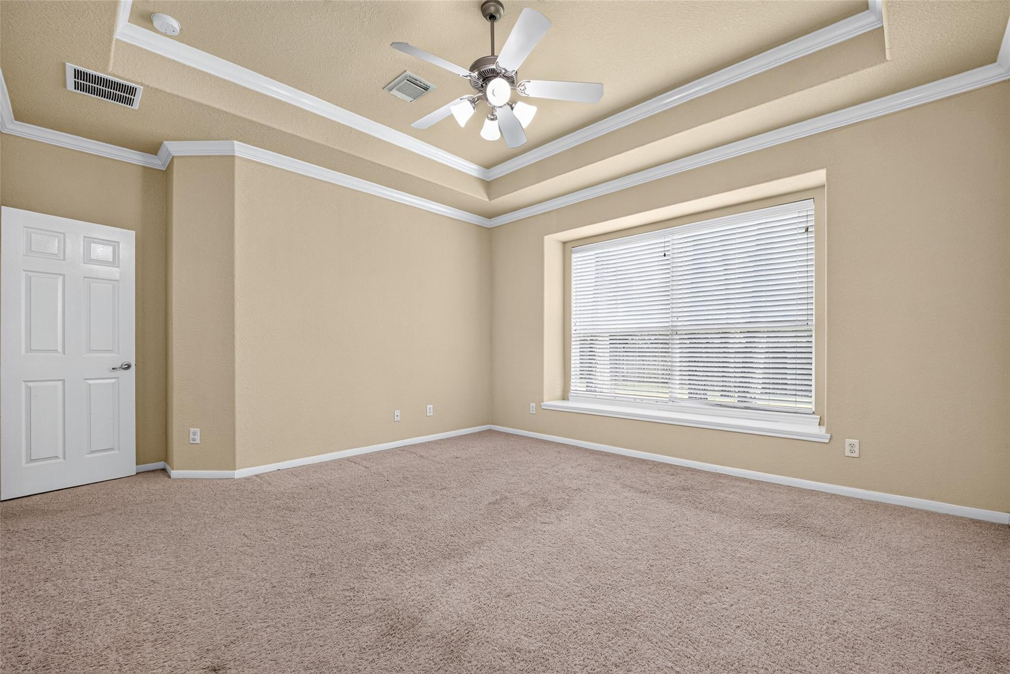 Empty bedroom with a tray ceiling, ceiling fan, carpet, and large window with blinds.