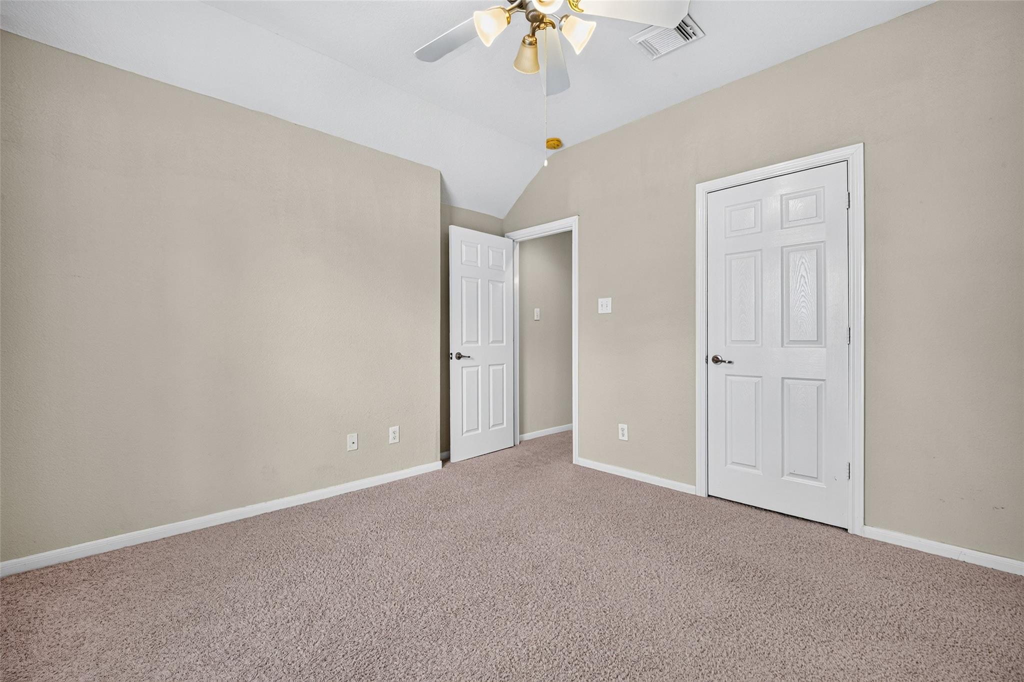 Empty carpeted bedroom with a vaulted ceiling, ceiling fan, and two white doors.