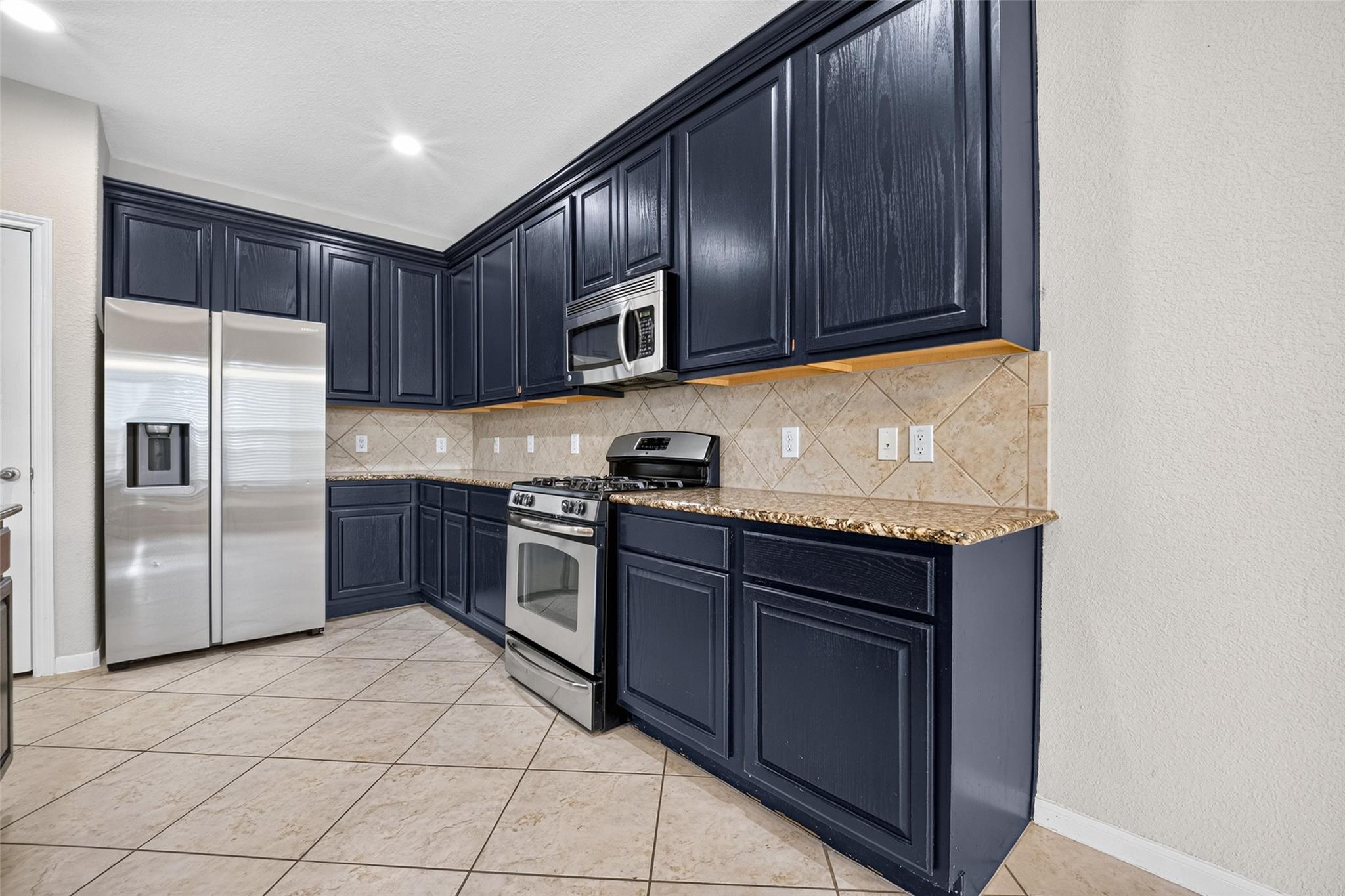 Kitchen with navy cabinets, stainless steel appliances, granite countertops, and beige tile backsplash.