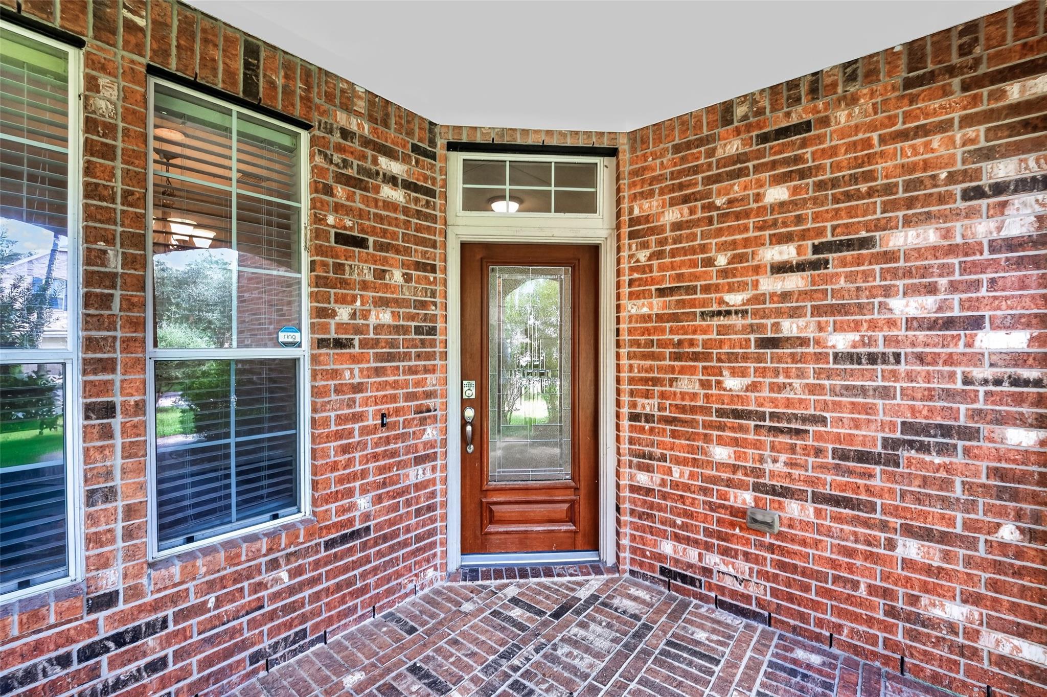 Brick-covered front entry with a wooden glass-panel door, brick paving, and windows with blinds.