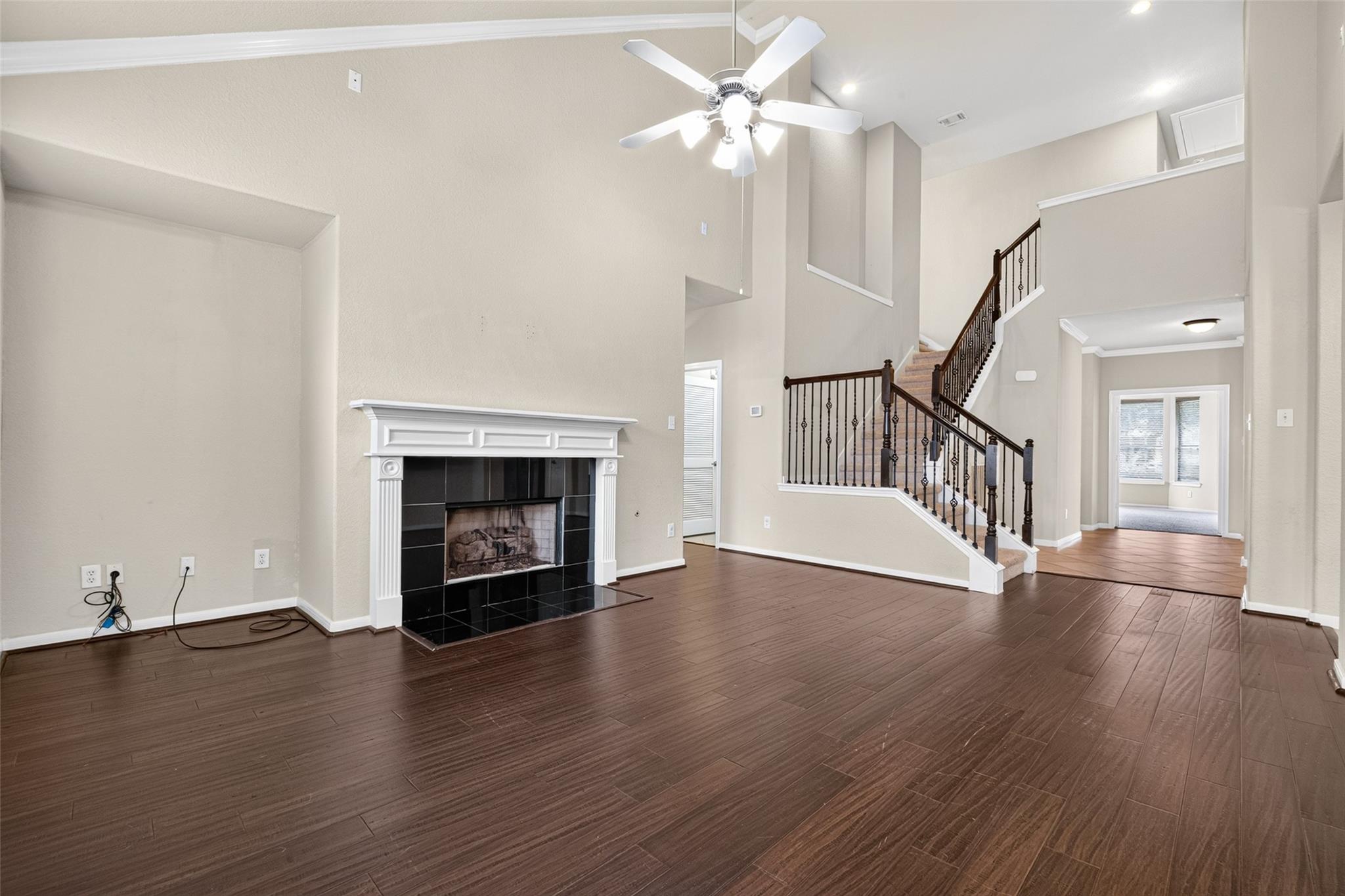 Empty two-story living room with a fireplace, dark wood flooring, and a staircase with iron railings.