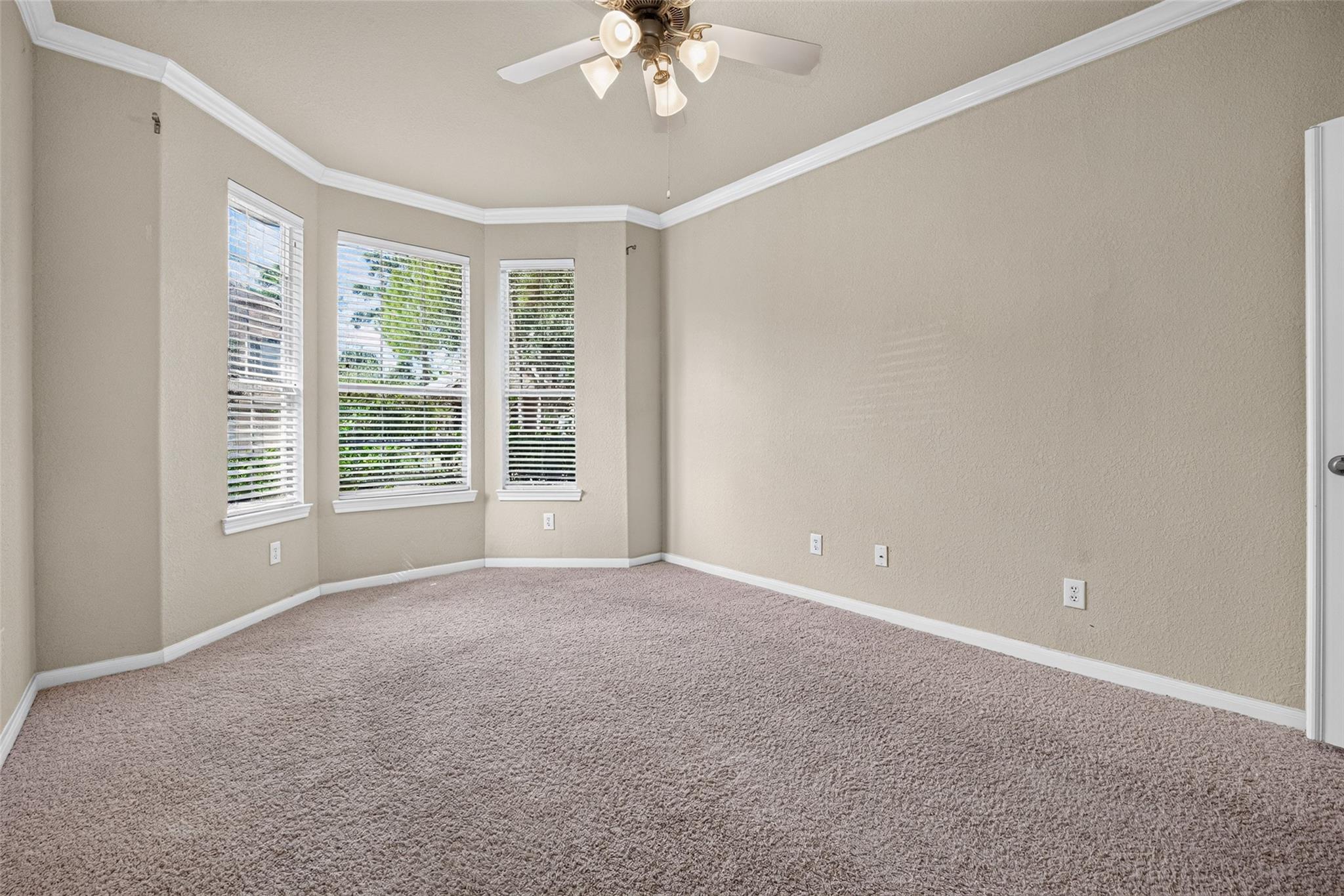 Empty carpeted bedroom with three windows and a ceiling fan.