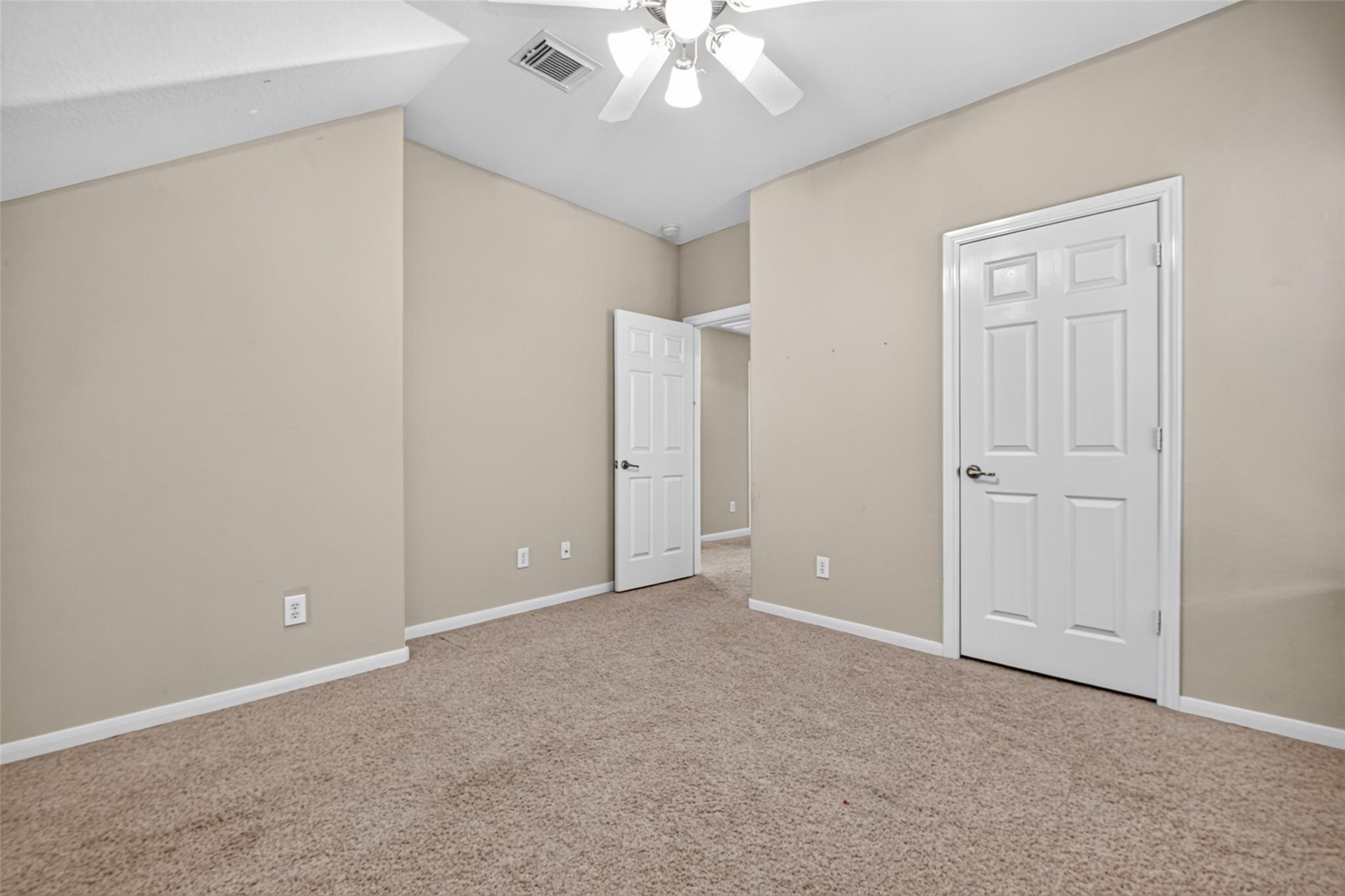Empty carpeted bedroom with beige walls, two white doors, and a ceiling fan.