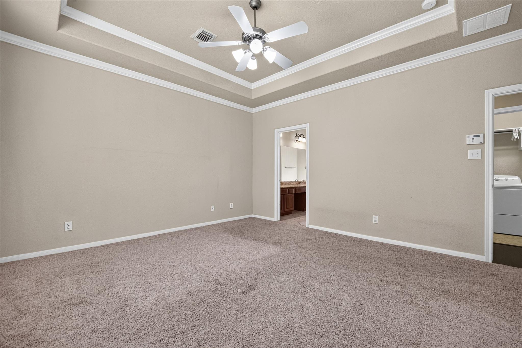 Unfurnished bedroom with a tray ceiling, carpet, and doorways to a bathroom and laundry area.