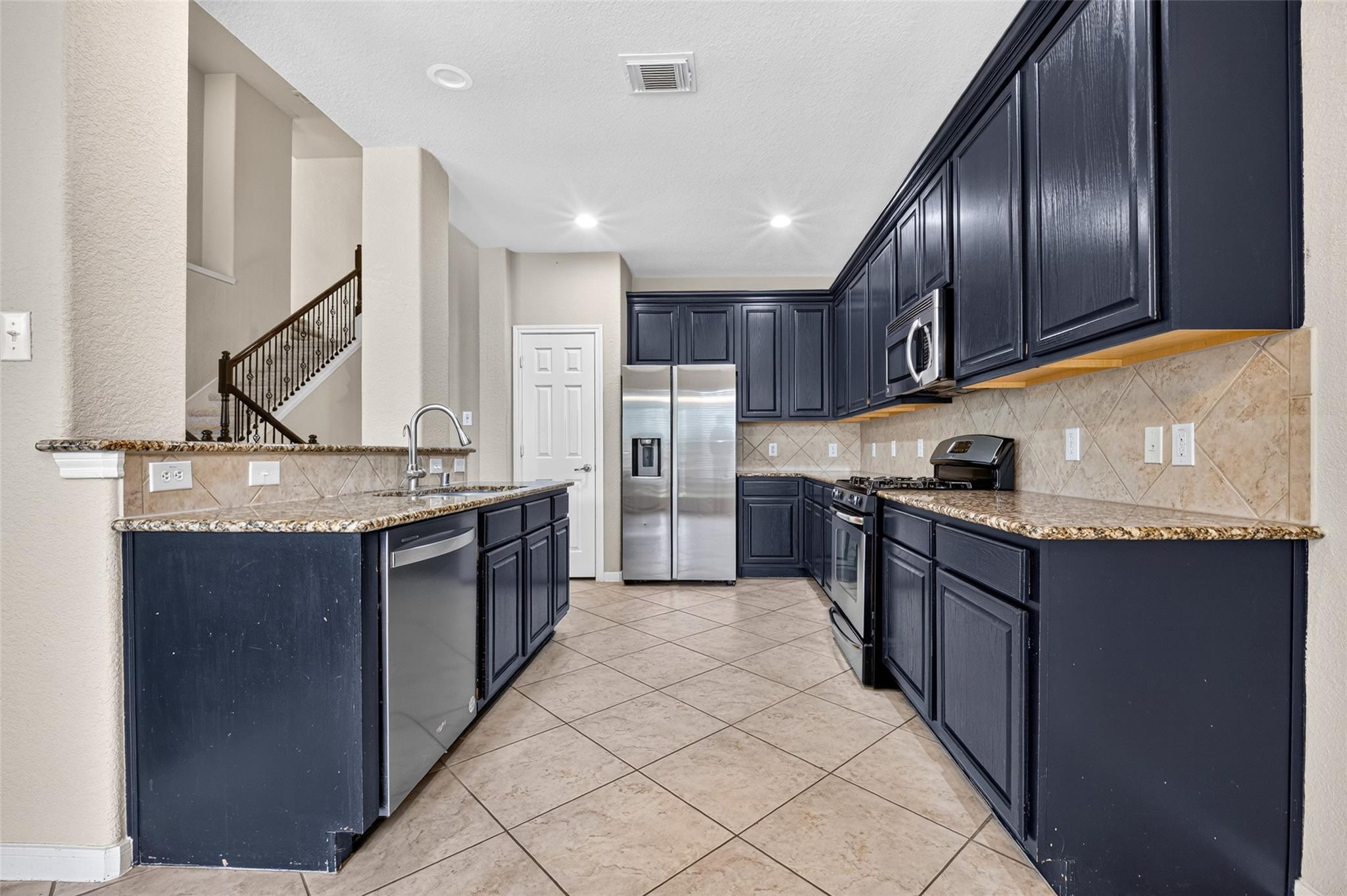 Kitchen with navy cabinets, granite counters, stainless steel appliances, and a peninsula sink.