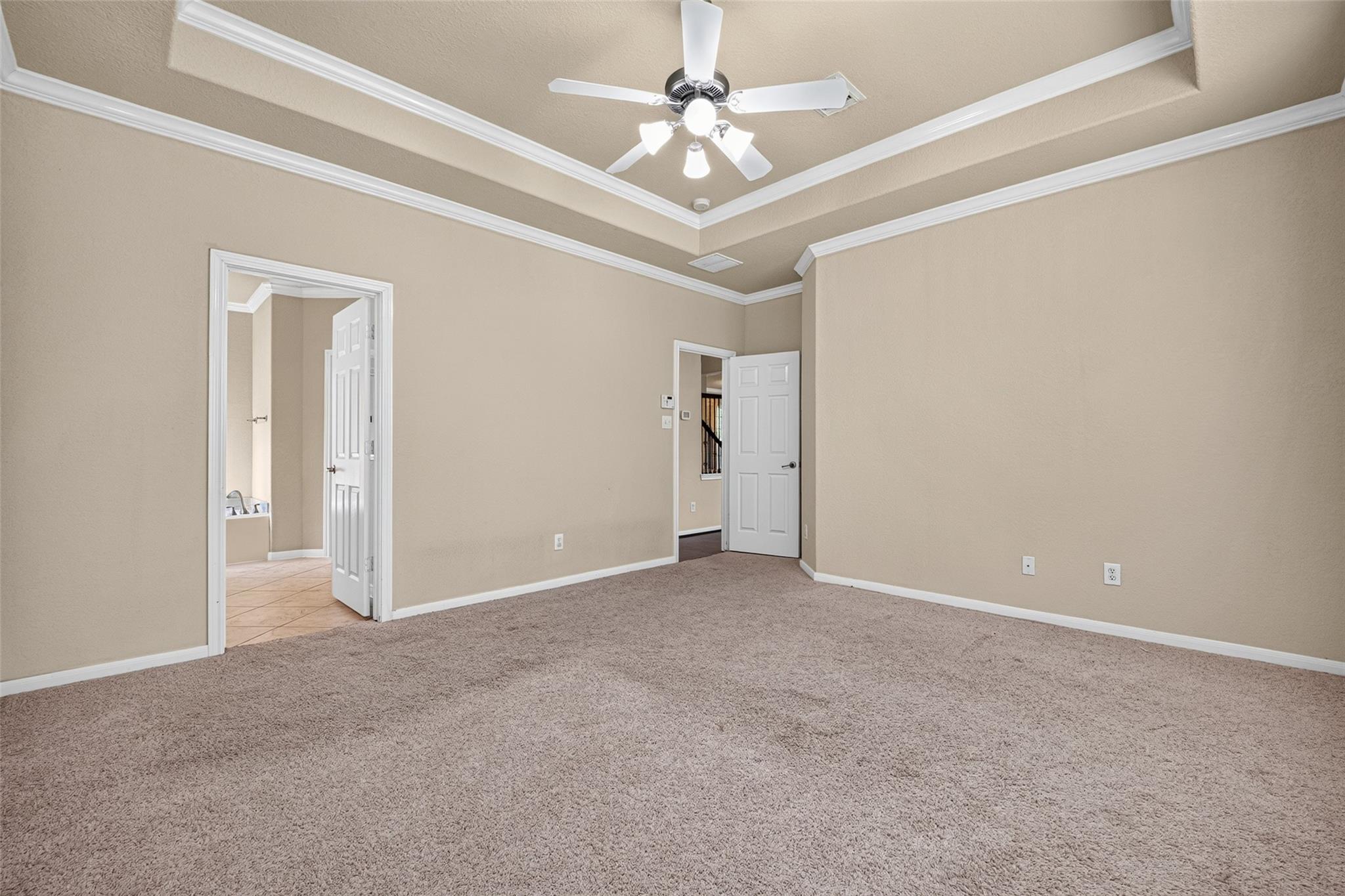 Empty carpeted room with beige walls, a tray ceiling, and a ceiling fan.