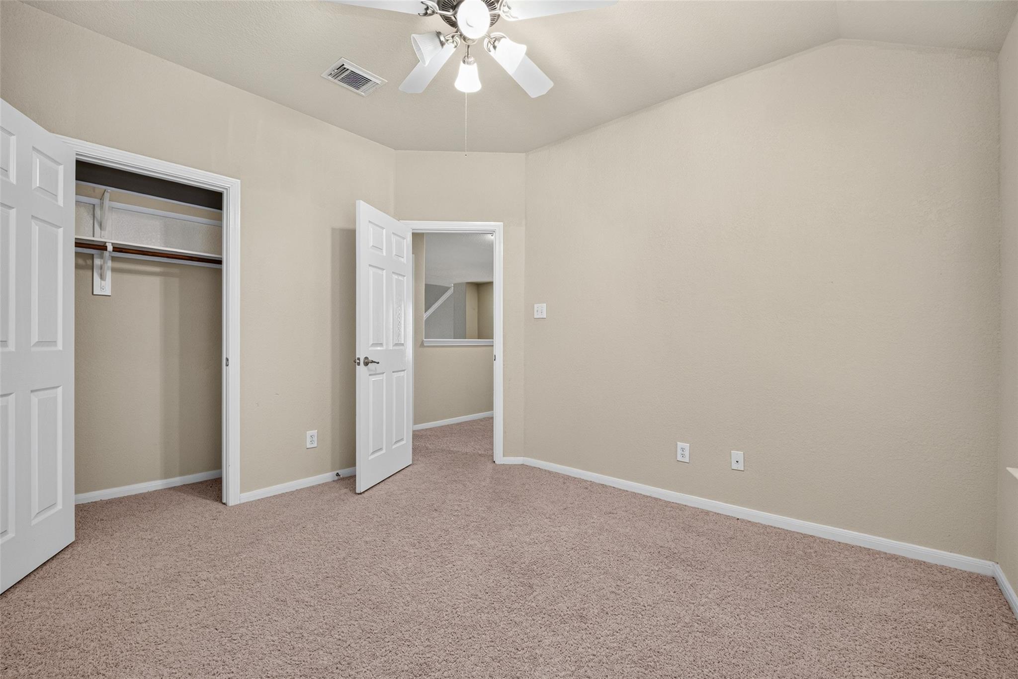 Empty carpeted bedroom with beige walls, an open closet, and a ceiling fan.