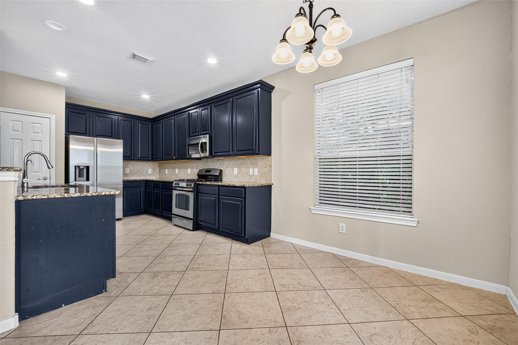Kitchen with navy cabinets, granite counters, stainless steel appliances, and large tile flooring.