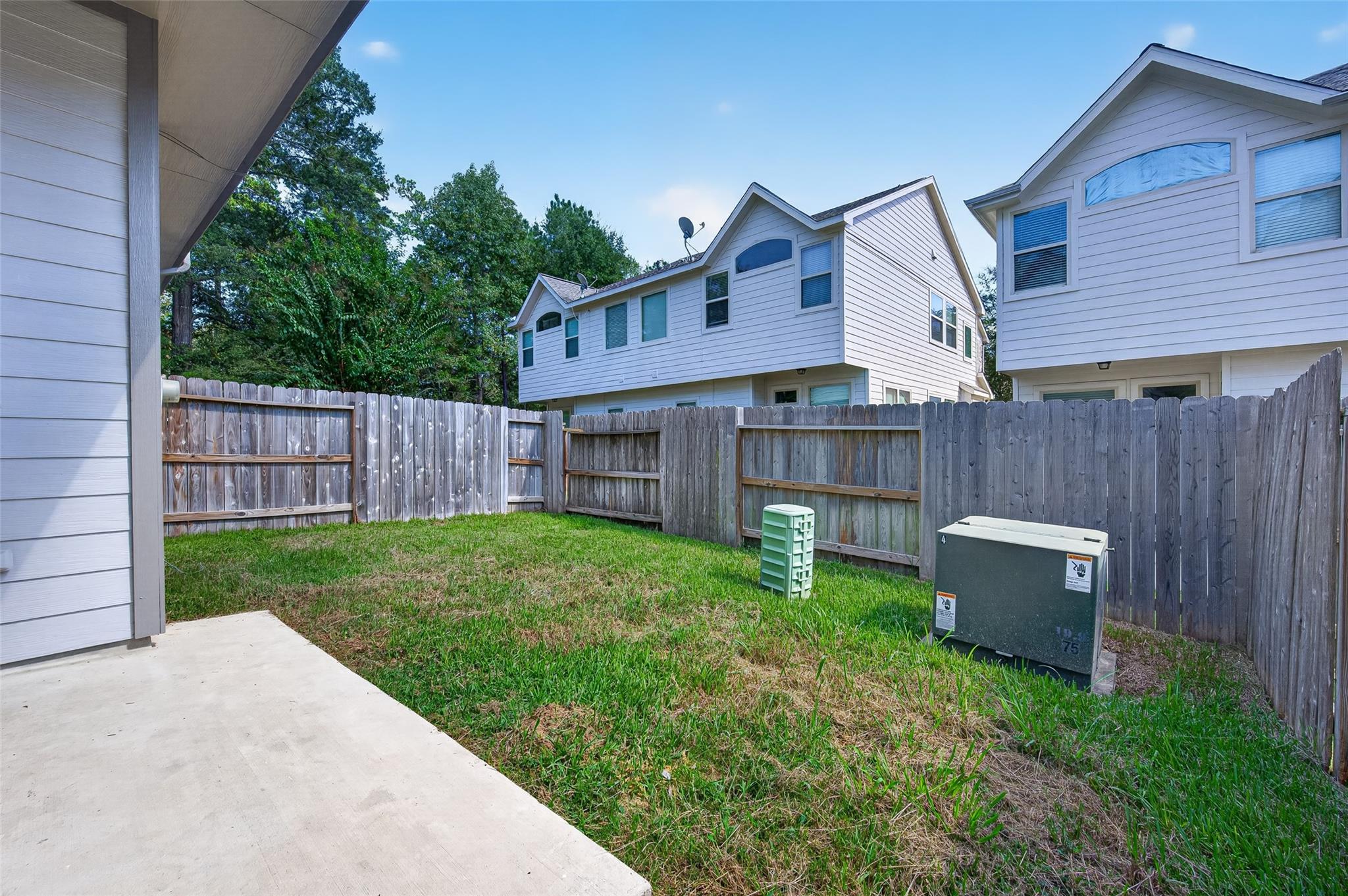 Fenced backyard with a grassy lawn, concrete patio, and utility equipment.