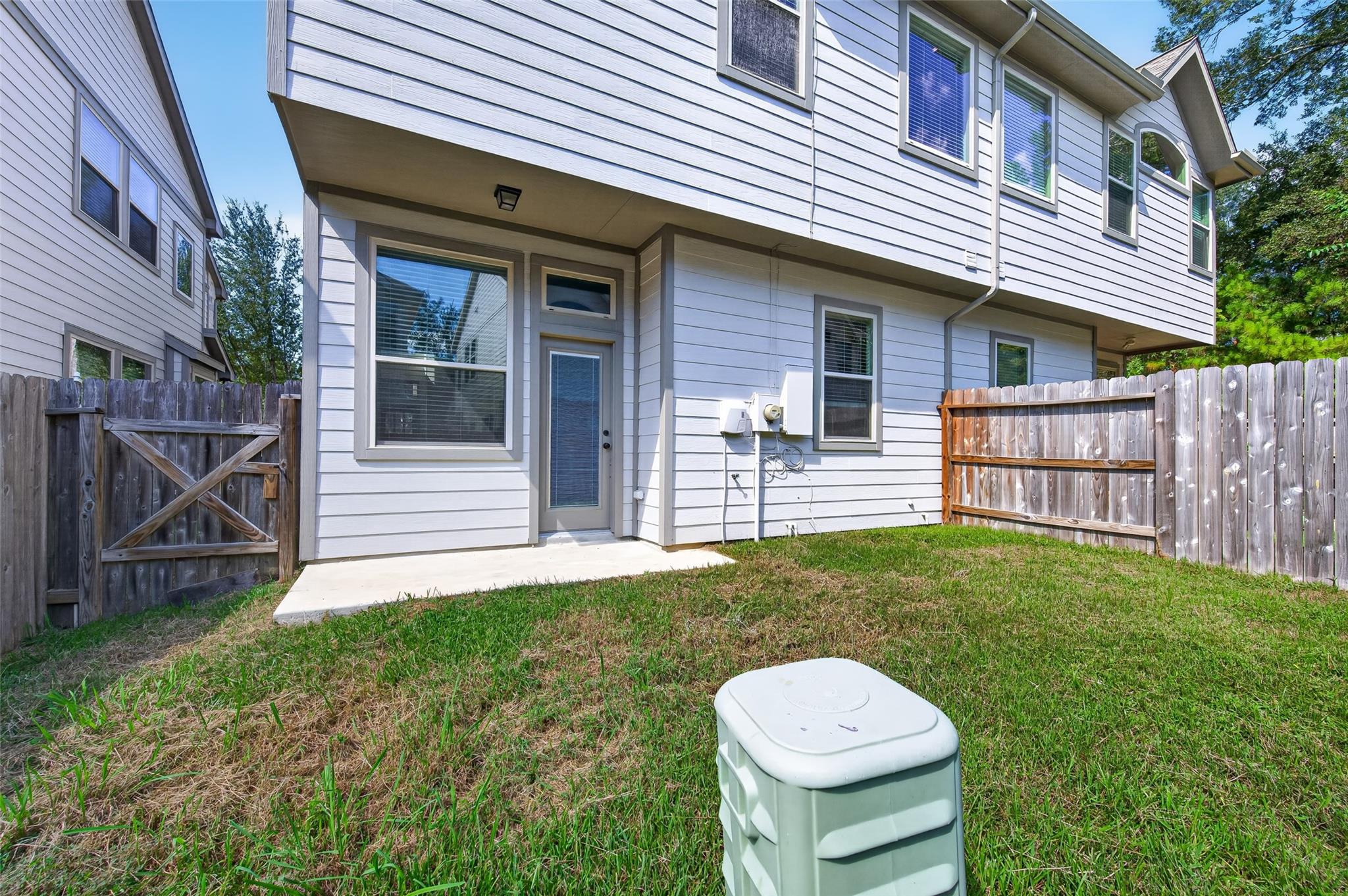 Rear of a two-story gray-sided home with a fenced yard and small patio.
